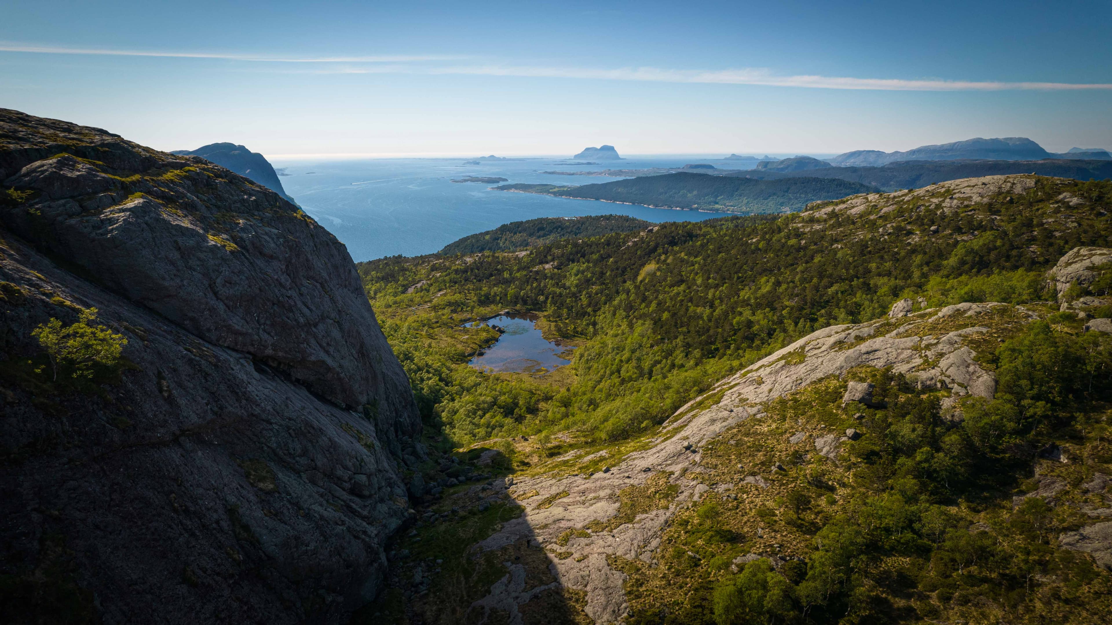 Vi ser nedover eit skar der det ligg eit lite vatn. Det er mykje skog rundt vatnet. Foto