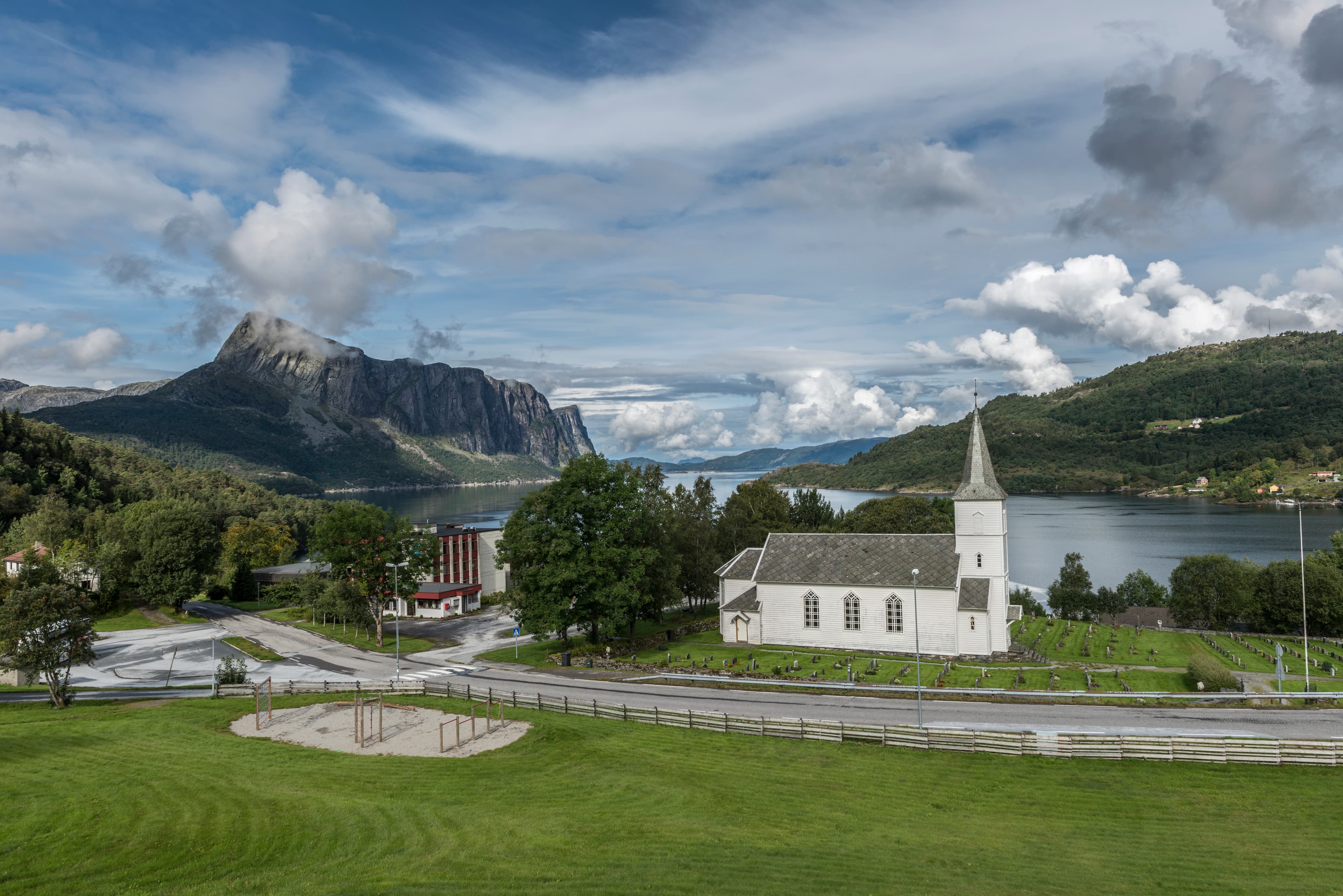 Hyllestad kyrkje er ei kvit langkyrkje. Rundt kyrkja ligg gravplassen. På andre sida av vegen ligg ein leikeplass. Kyrkja ligg innerst i ein fjord og vi ser Lihesten steile seg ytterst i fjorden. Foto