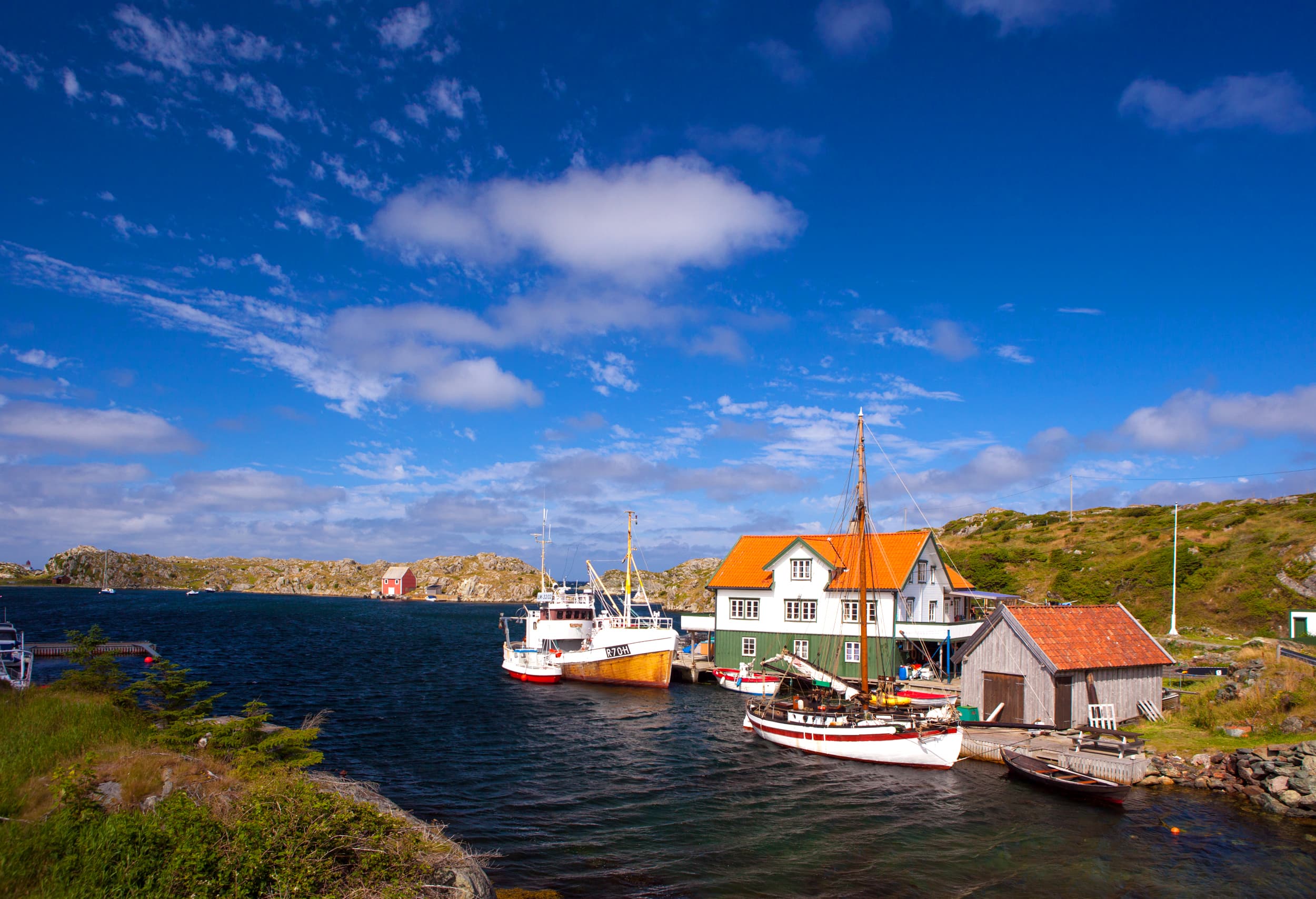 Båter fortøyd ved en kai på Røvær, et hus og noen naust.