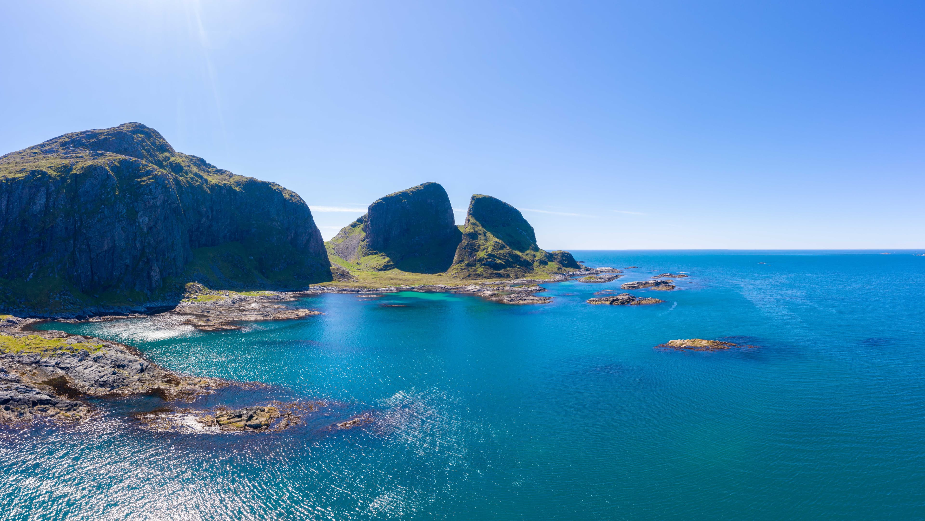 Dronebilde av Kinnaklova. Kinnaklova er ei kløft i eit fjell. Det er sol og blå himmel og vi ser utover havet. Foto
