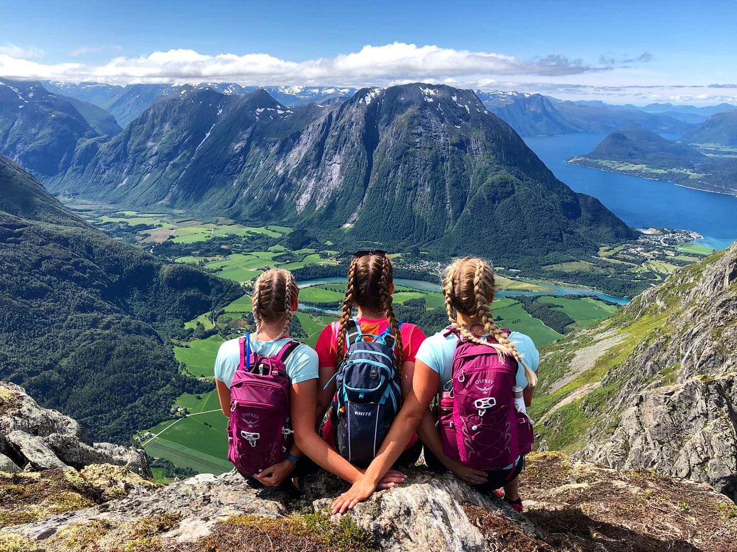 Tre jenter med fletter som sitter med ryggen til og ser på utsikten fra Romsdalseggen.