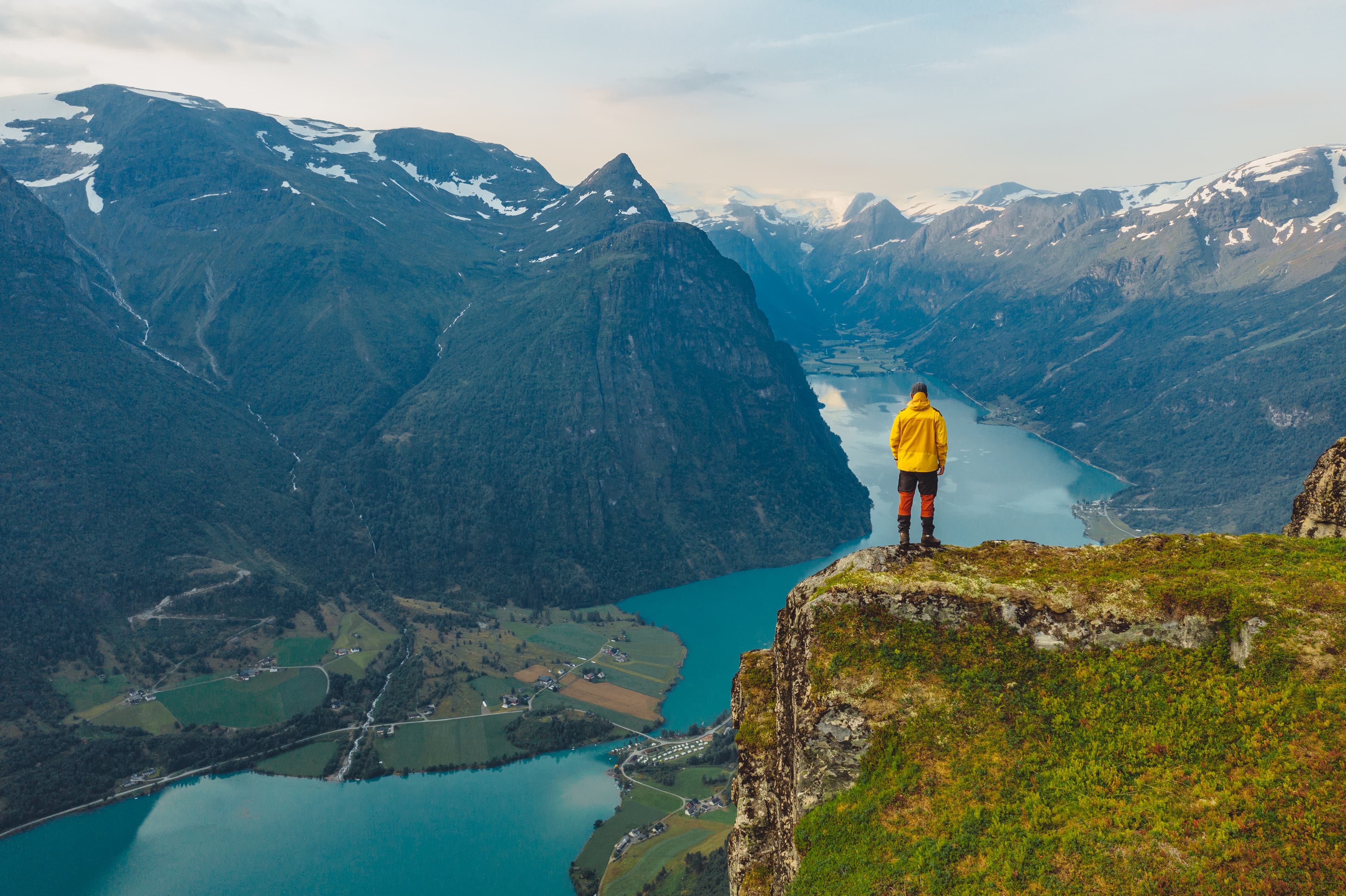 En mann som står med ryggen til og ser utover et storslått landskap med høye fjell og en vann nedenfor.