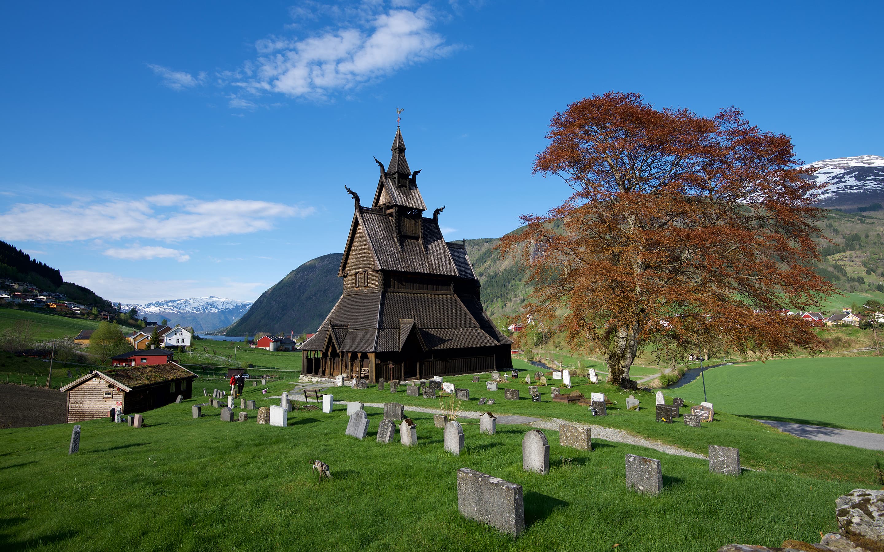 Hopperstad stavkirke med gravstøtter i forgrunnen og utsikt nedover dalen mot fjorden.