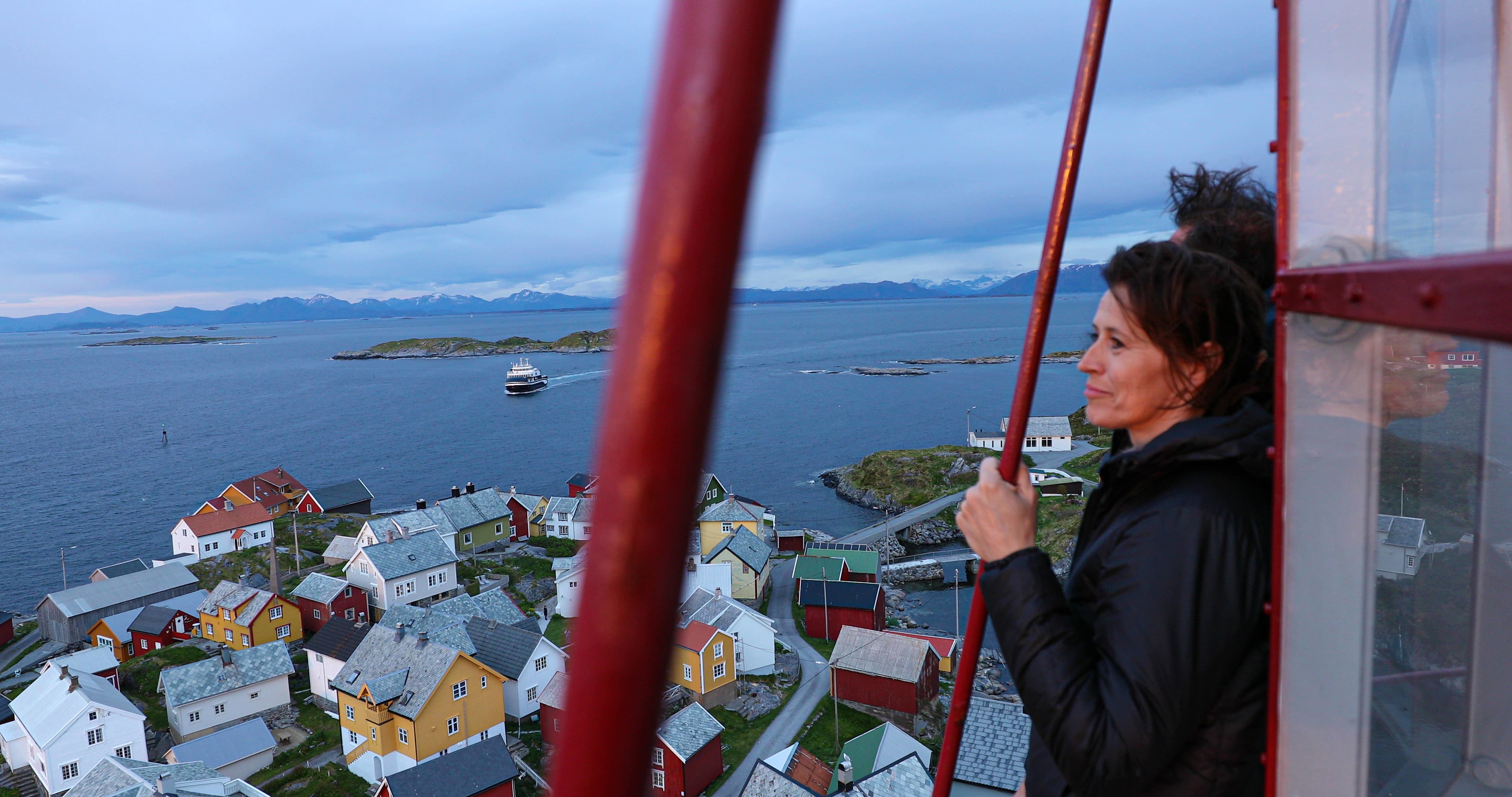 Par står oppe i fyret på Ona, ser ned på de fargerike husene og ferga som kommer og skal legge til kai.
