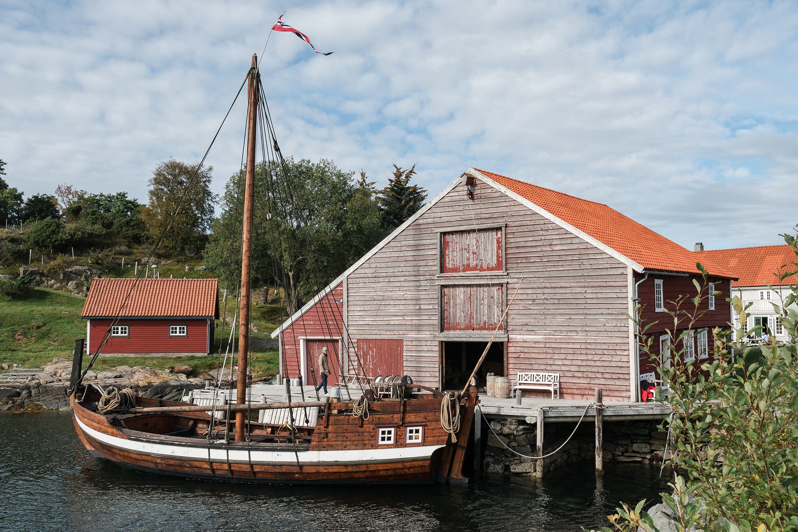 Gammal båt ligg ved kai og naust på museumet Herøy Gard.