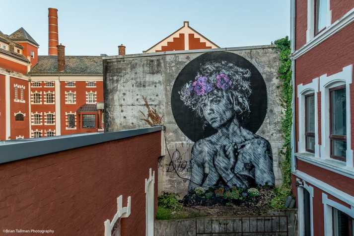 Et veggmaleri av en kvinne med krans av blomster i håret, og en svart sirkel malt bak hodet.