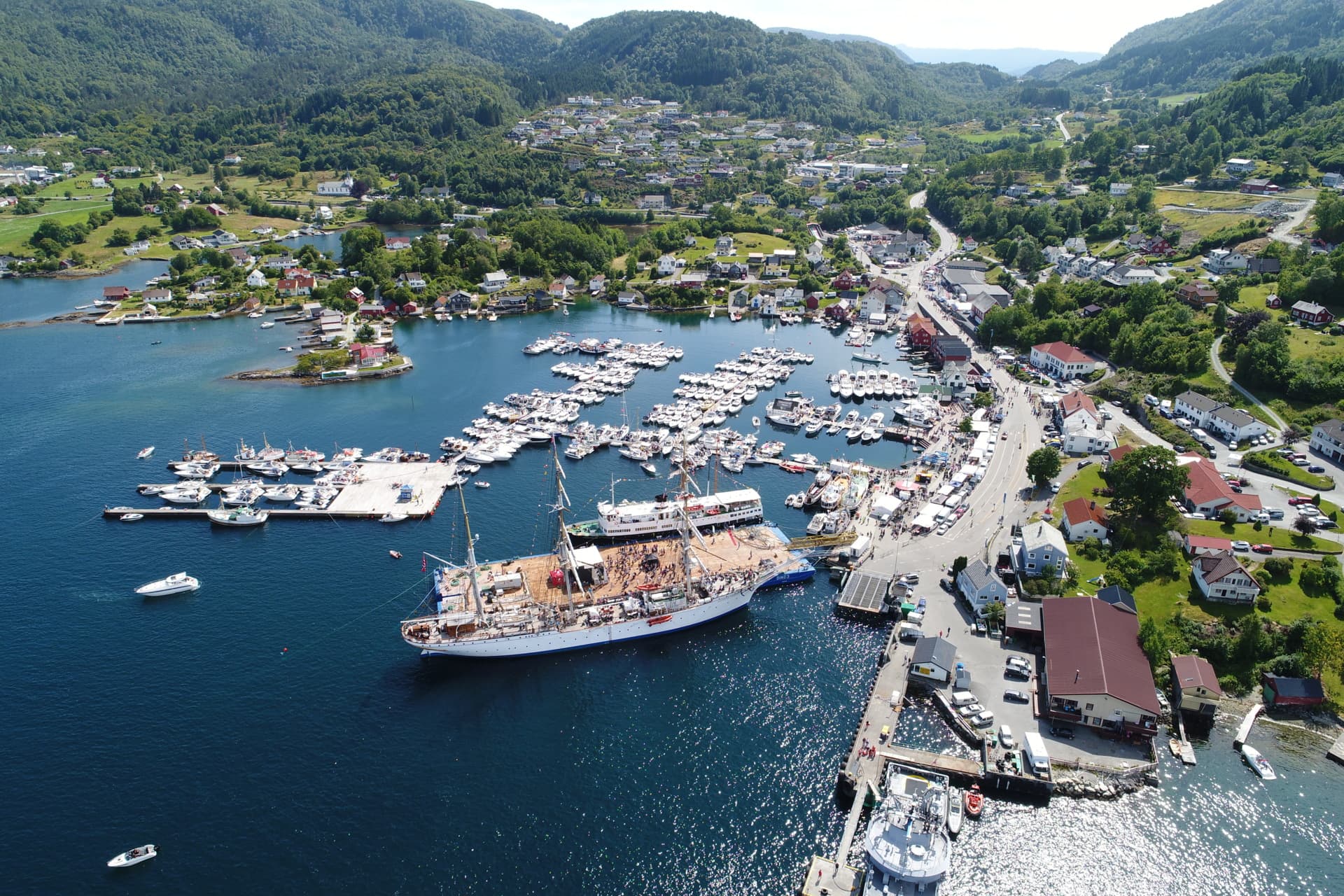 Mange fritidsbåter og en stor seilskute til kai, sett fra luften.