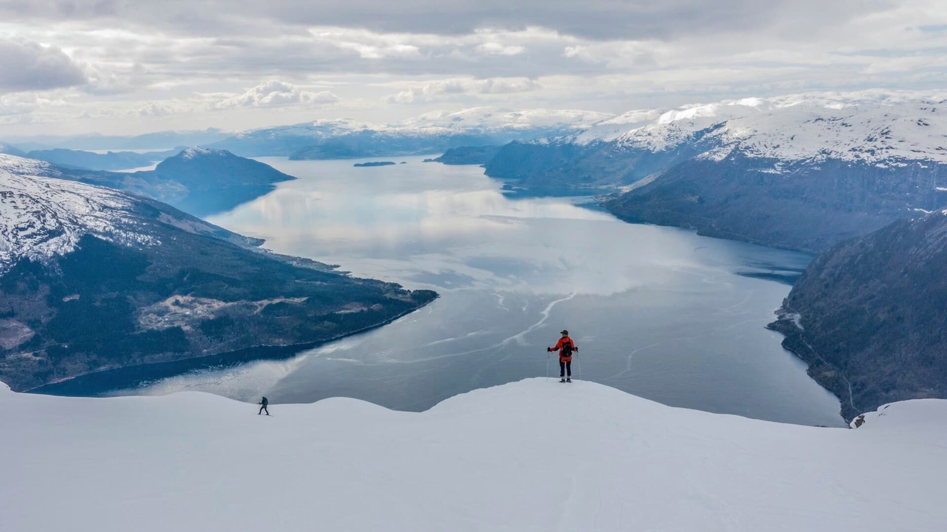 To personer på ski et stykke unna, med storslått utsikt over fjorden og fjellene rundt.