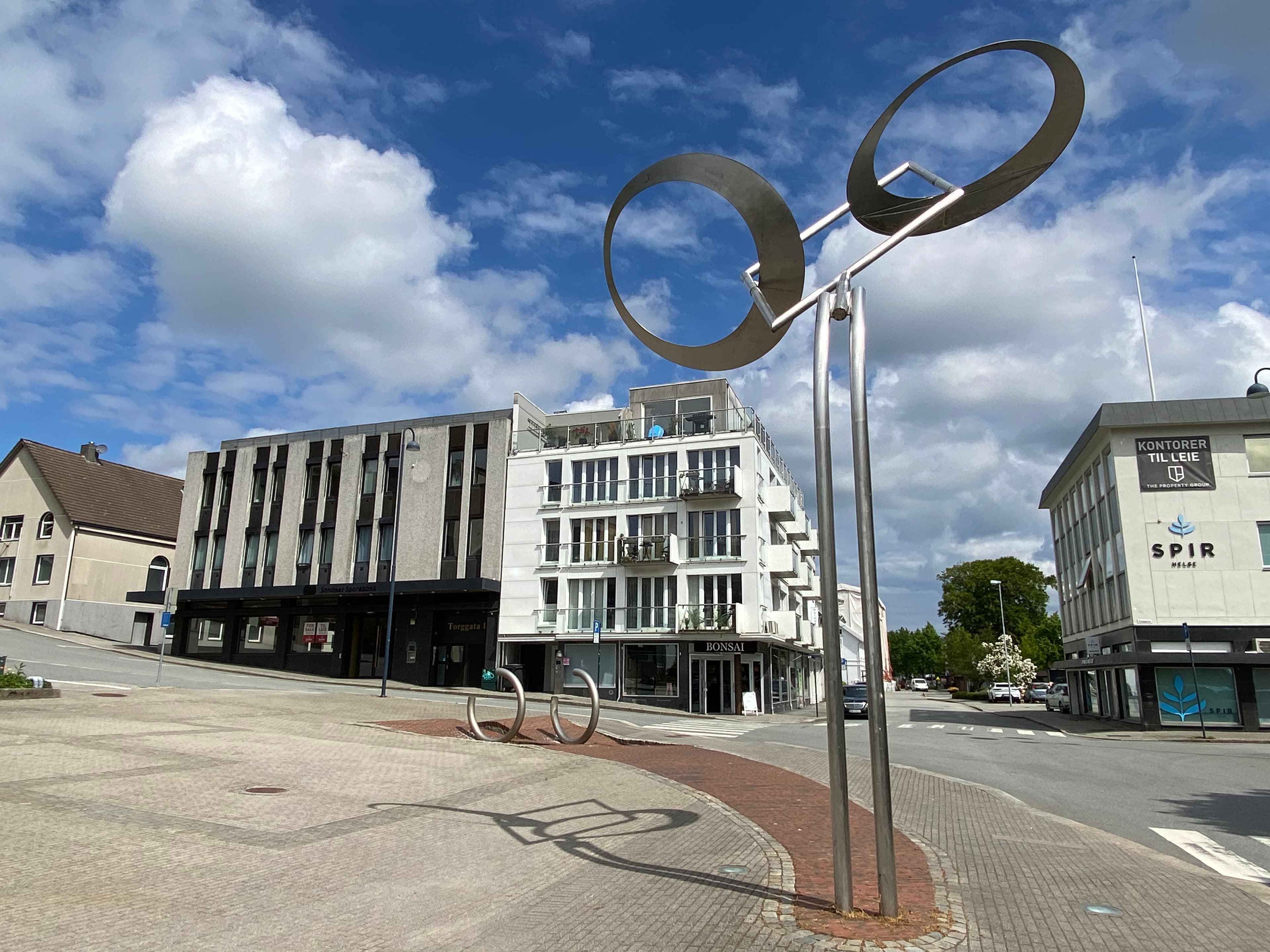 Av sted signert Reinhard Haverkamp, 2001. Bevegelig skulptur med to metallringer som endrer posisjon mot de brutte ringene på bakken. En abstraksjon av å være i full fart, kanskje sykle?