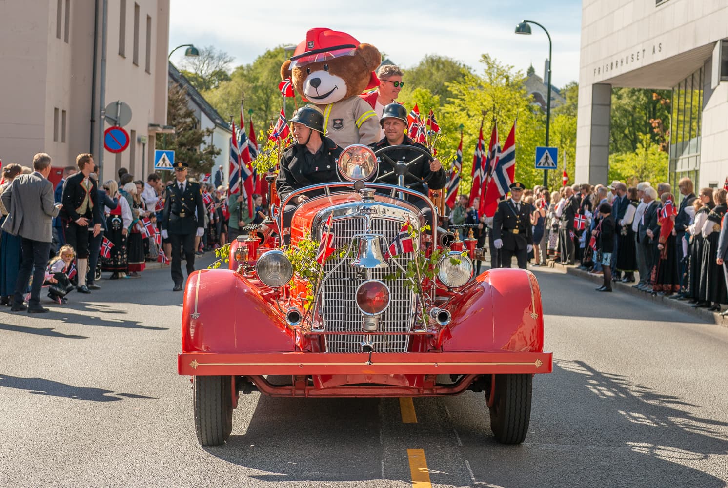 Old fashioned fire truck with large teddy bear and kids on board travelling past crowds on constitution day in stavanger. Norwegian flags everywhere.