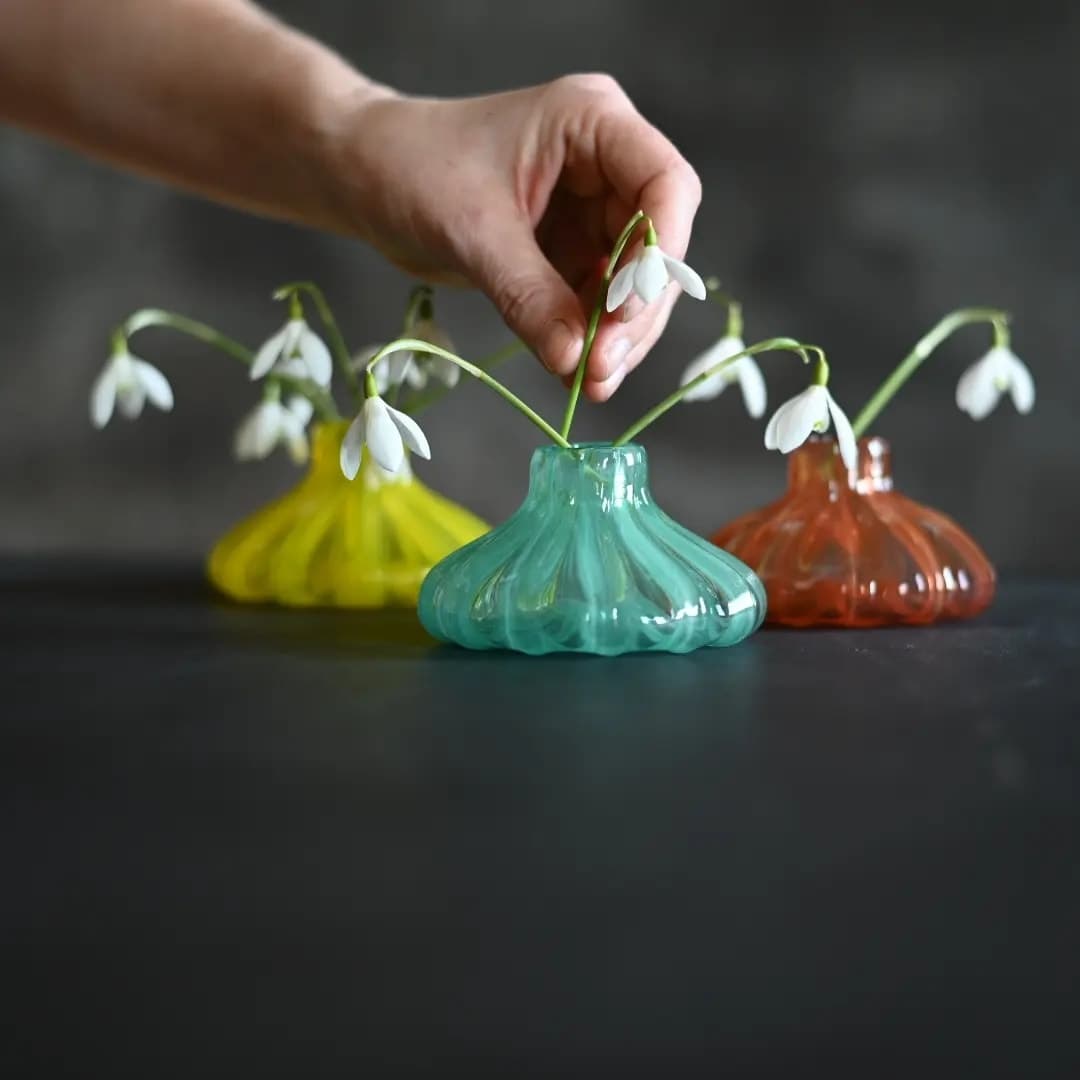 Tre vaser i glass i gul, grønn og oransje med snøklokker i.