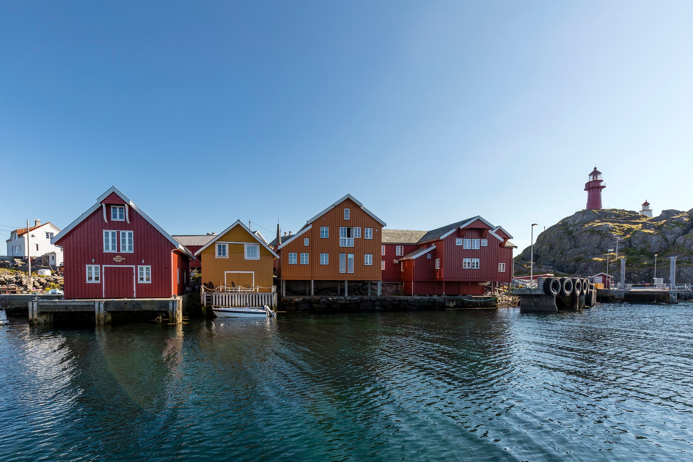 Røde og orange sjøhus på kaia på Ona med fyret i bakgrunn.
