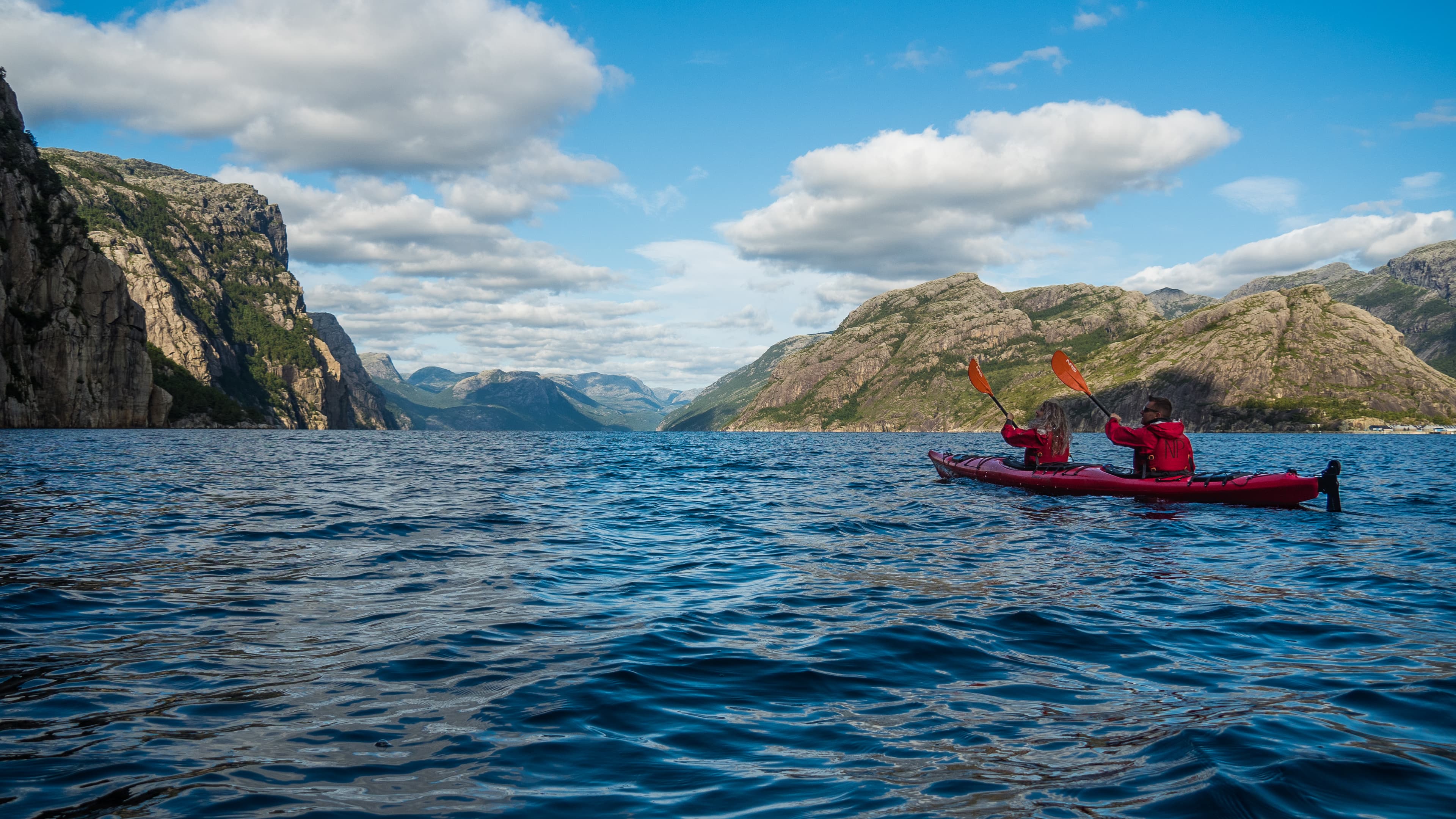 Tow people kayaking in the blue Lysefjord with mountains on each side