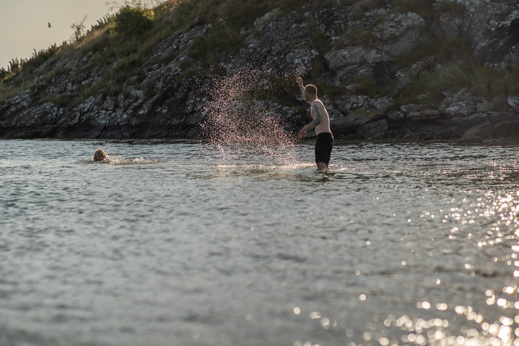 To personer som bader i en bukt på Kvitsøy. Solen glitrer i havet.