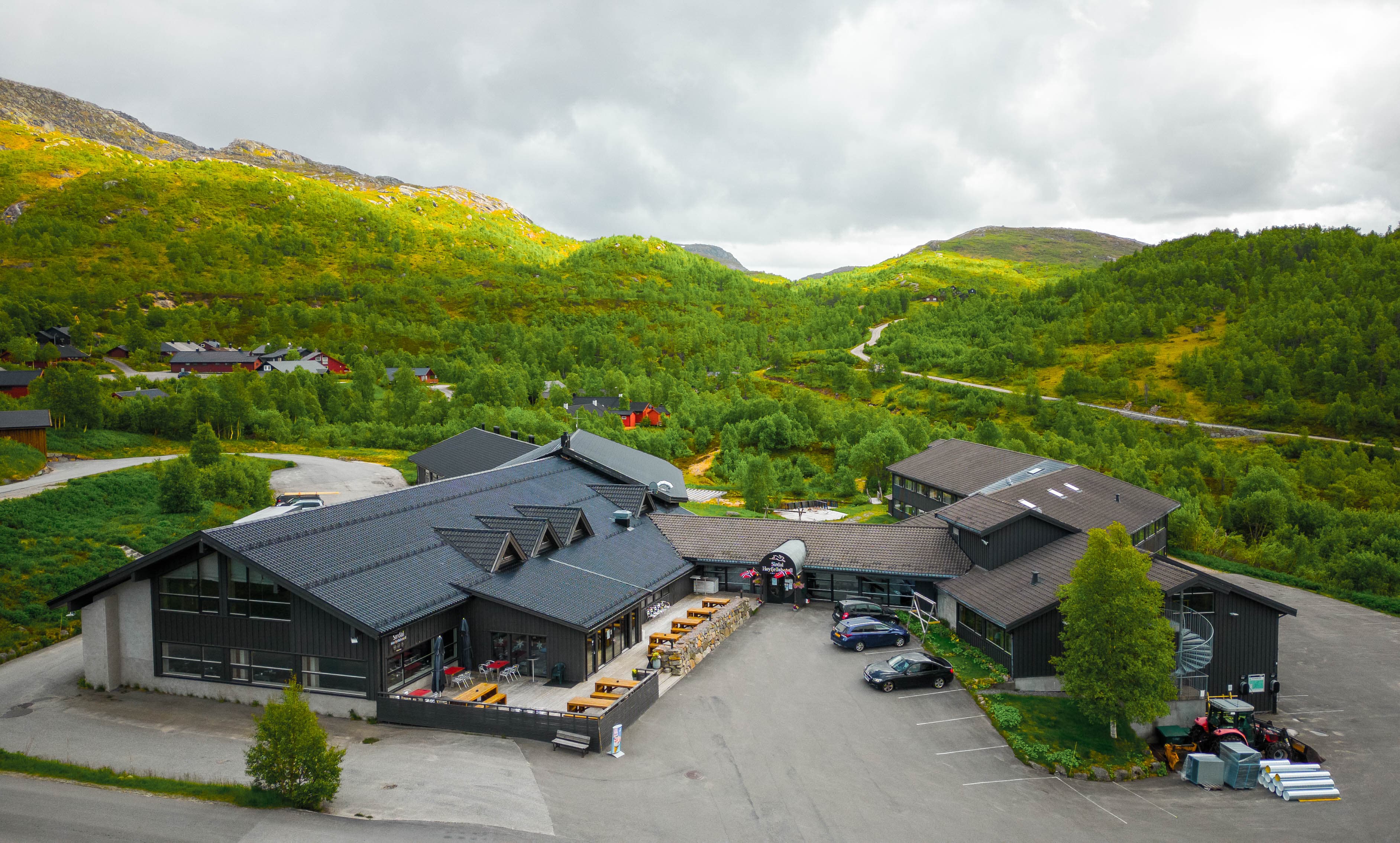 Dronebilde av hotell mellom grønnkledde fjell og marker.