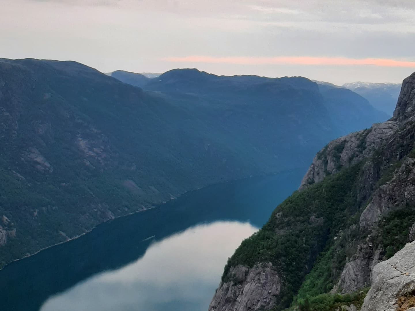 View from the mountain top towards steep mountains rising from the fjord