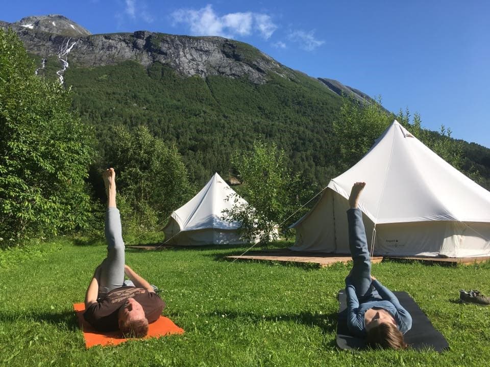 Folk ligger på grønt gress med glampingtelt i bakgrunnen, og gjør yoga.