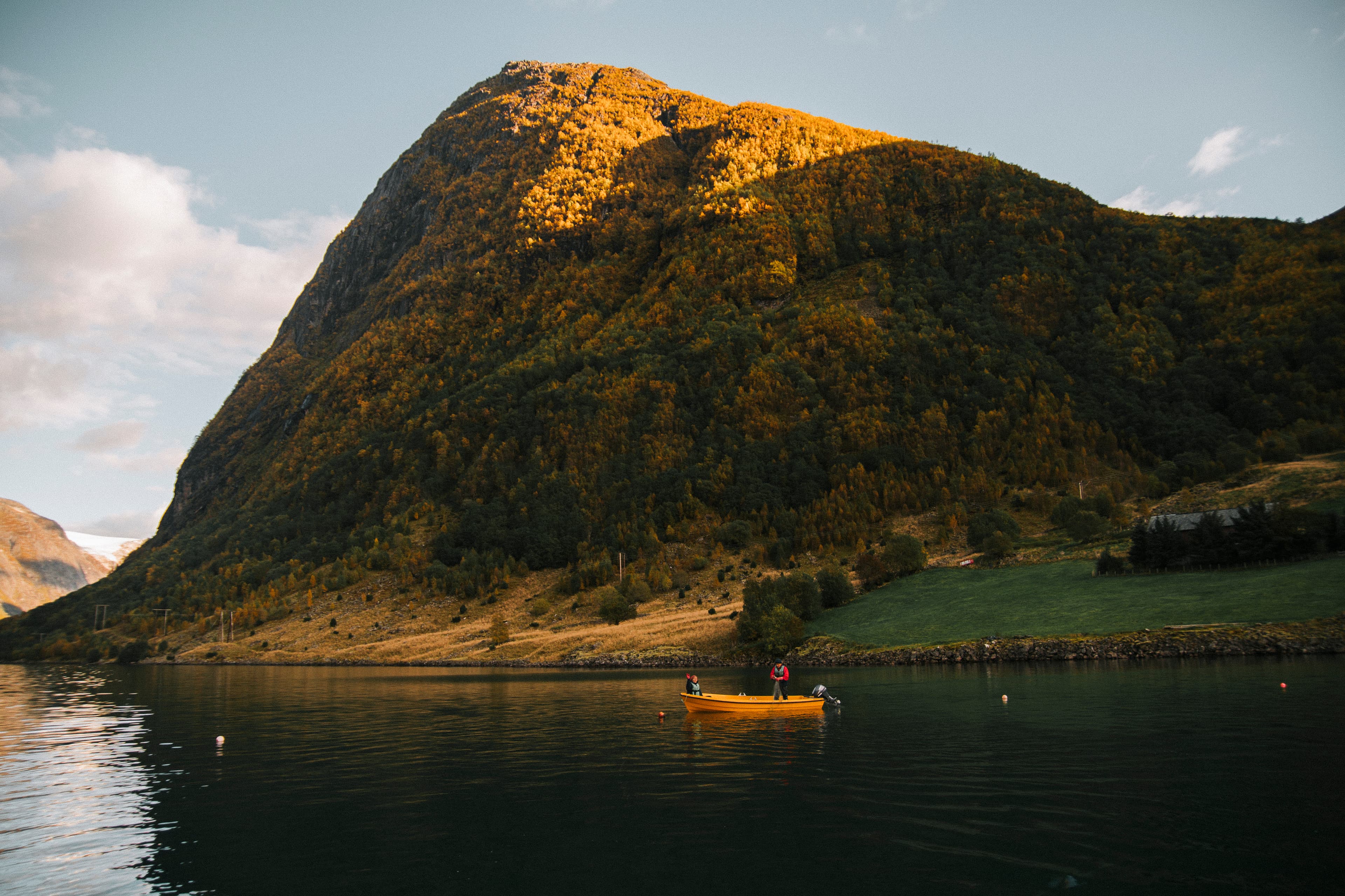 Båt ligg på fjorden og fiskar under stupbratte fjell.foto