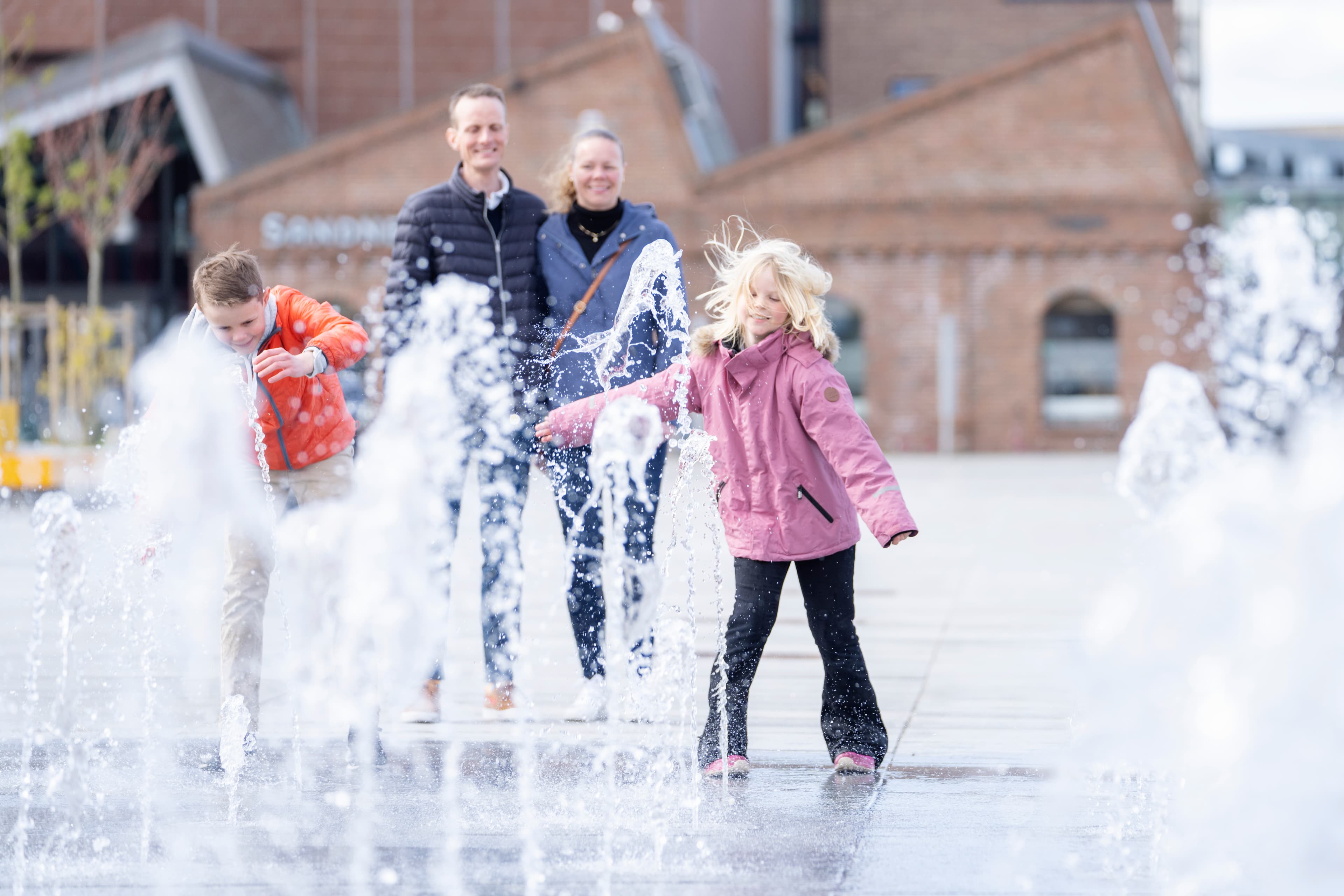 Familie på fire personer står og ser på fontene i Sandnes sentrum.