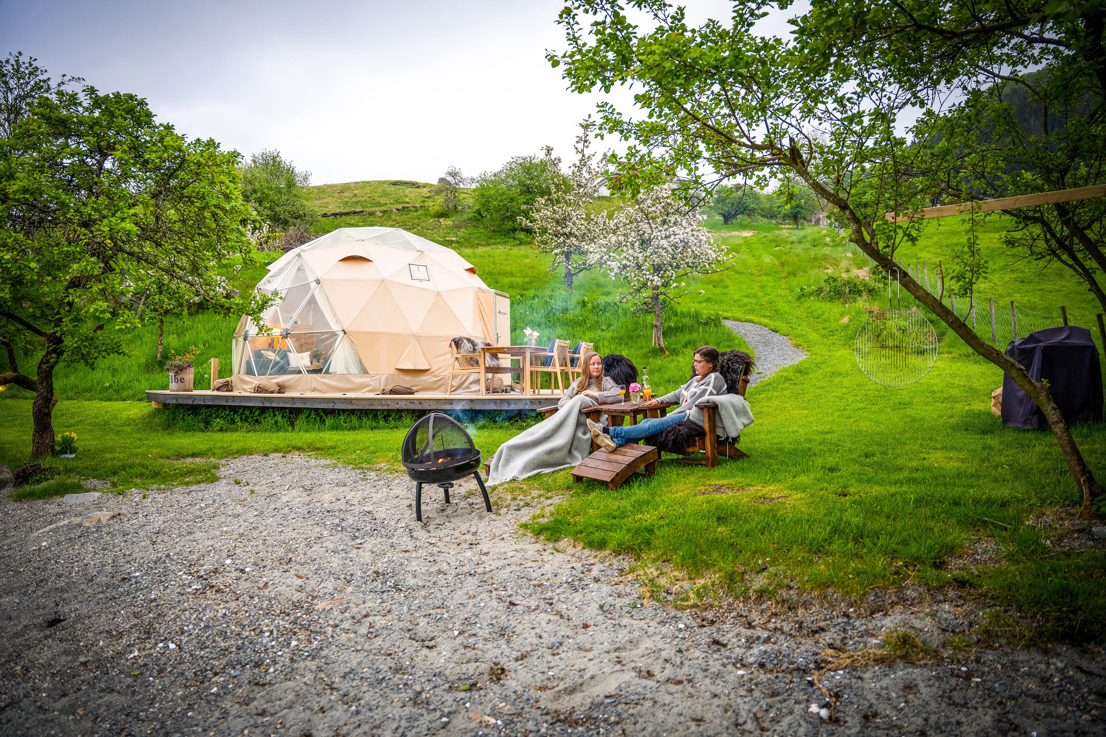 To personer som sitter utenfor glampingteltet med bålpanne og eplemost.