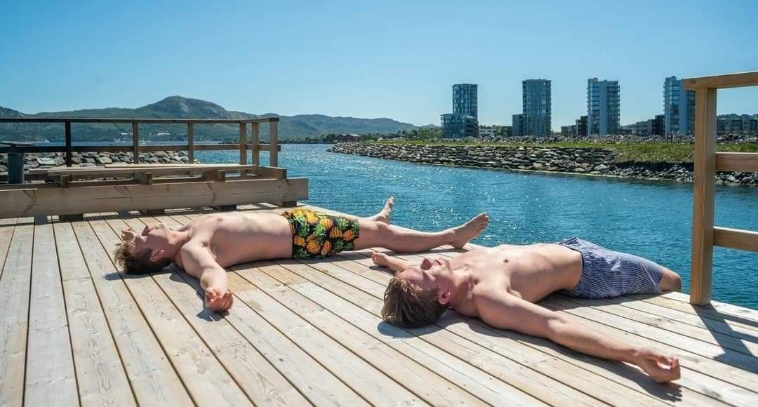 To gutter ligger på en brygge og soler seg i badebukser.