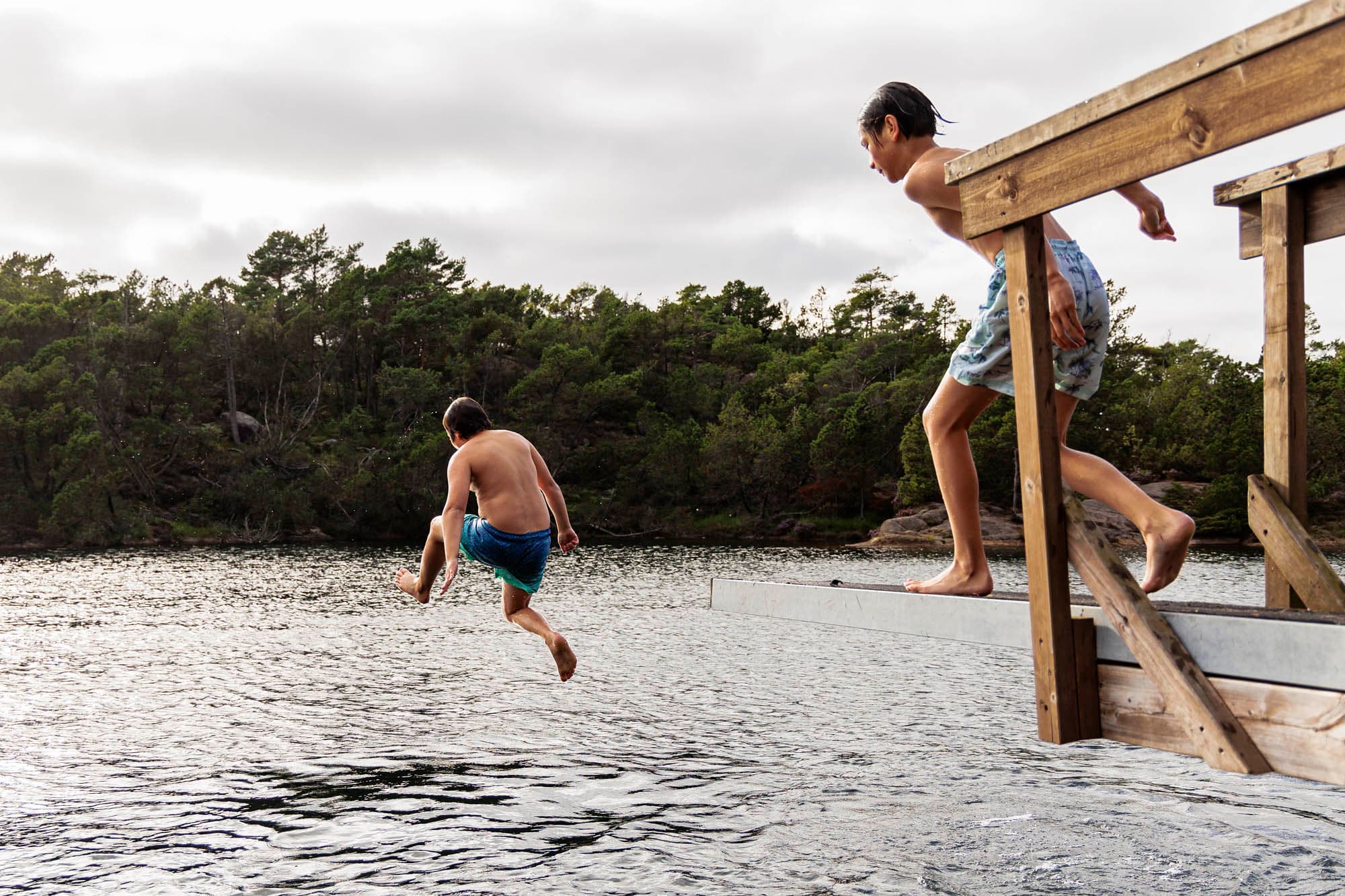 Two boys jump from a diving board into the lake