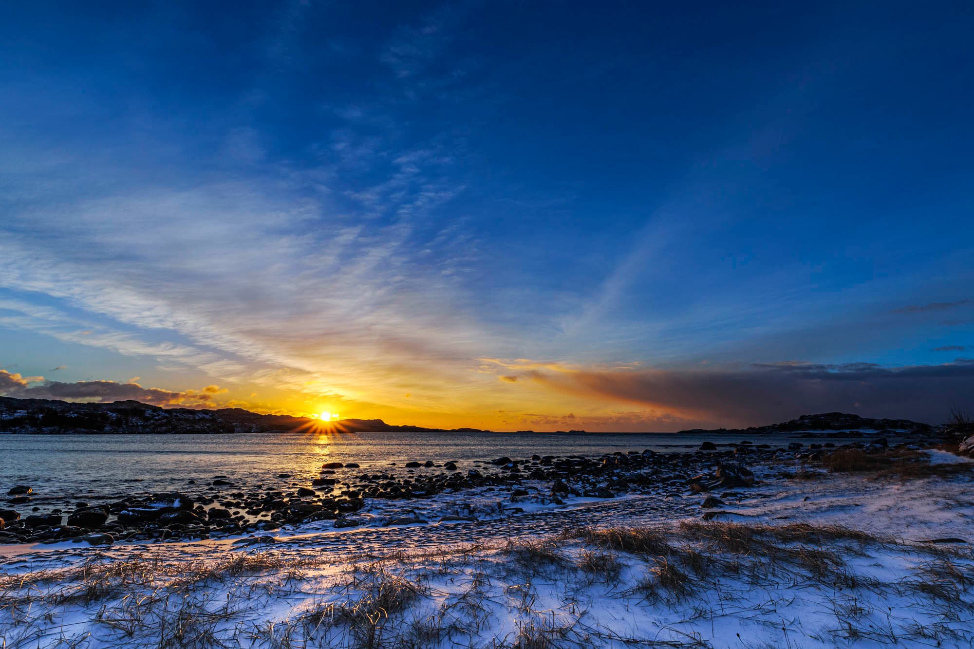 low winter sun at a beach, blue dark skies and orange sunset. beach with snow