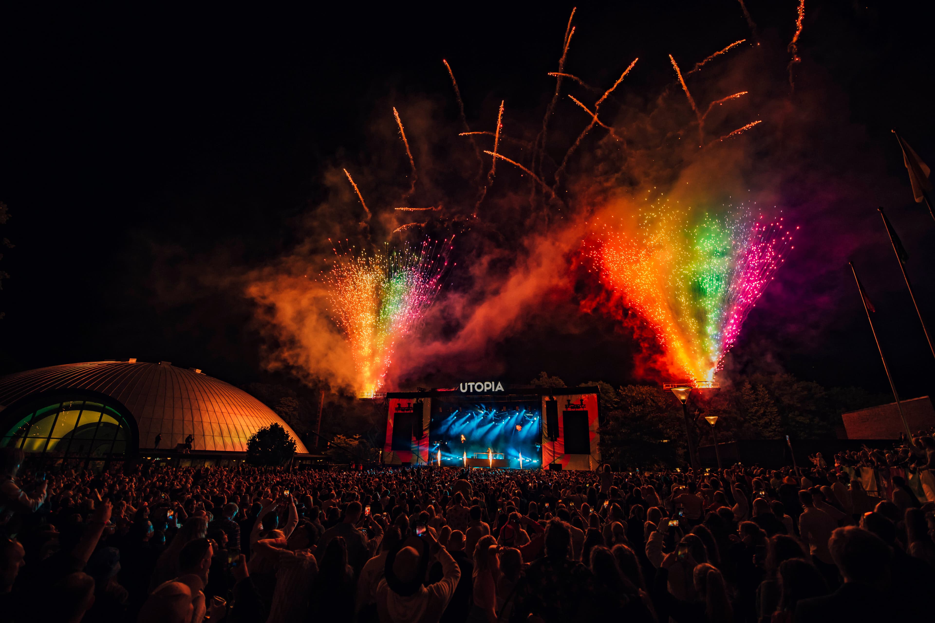 Festival stage at night with roaring audience and rainbow lights and fireworks