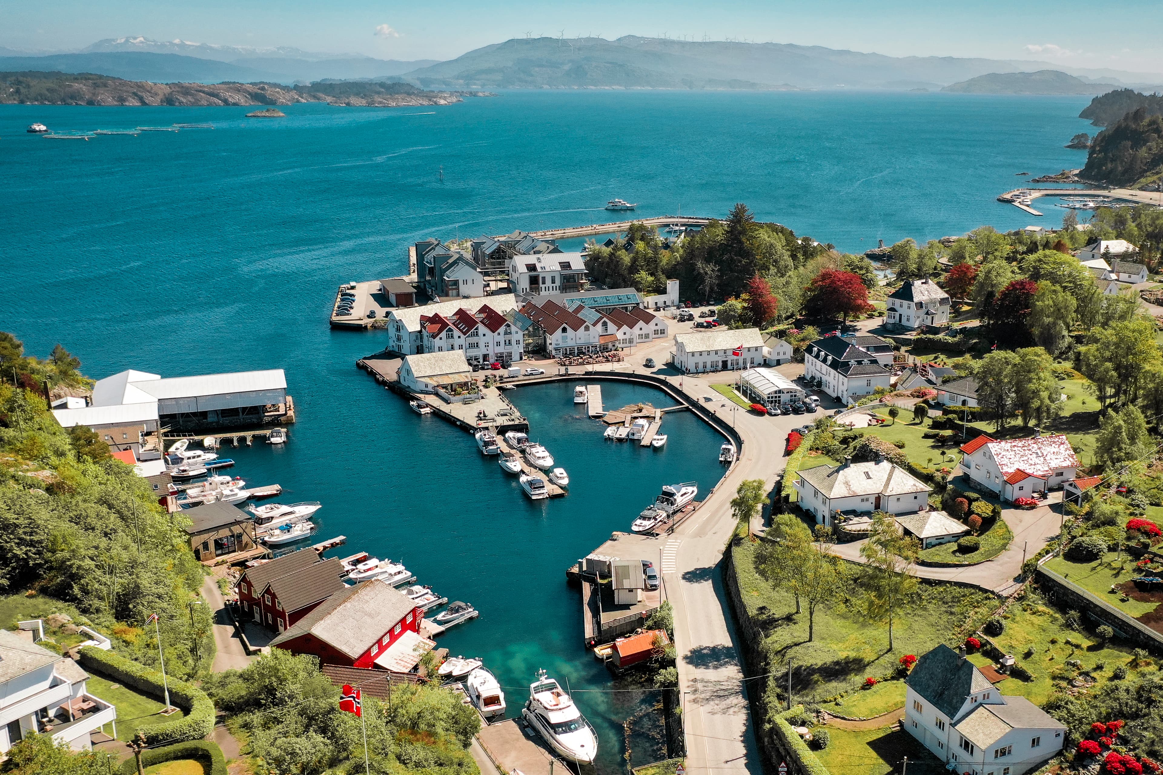 luftfoto over havn, hus, grøntarealer, fjord, fjell og båter.
