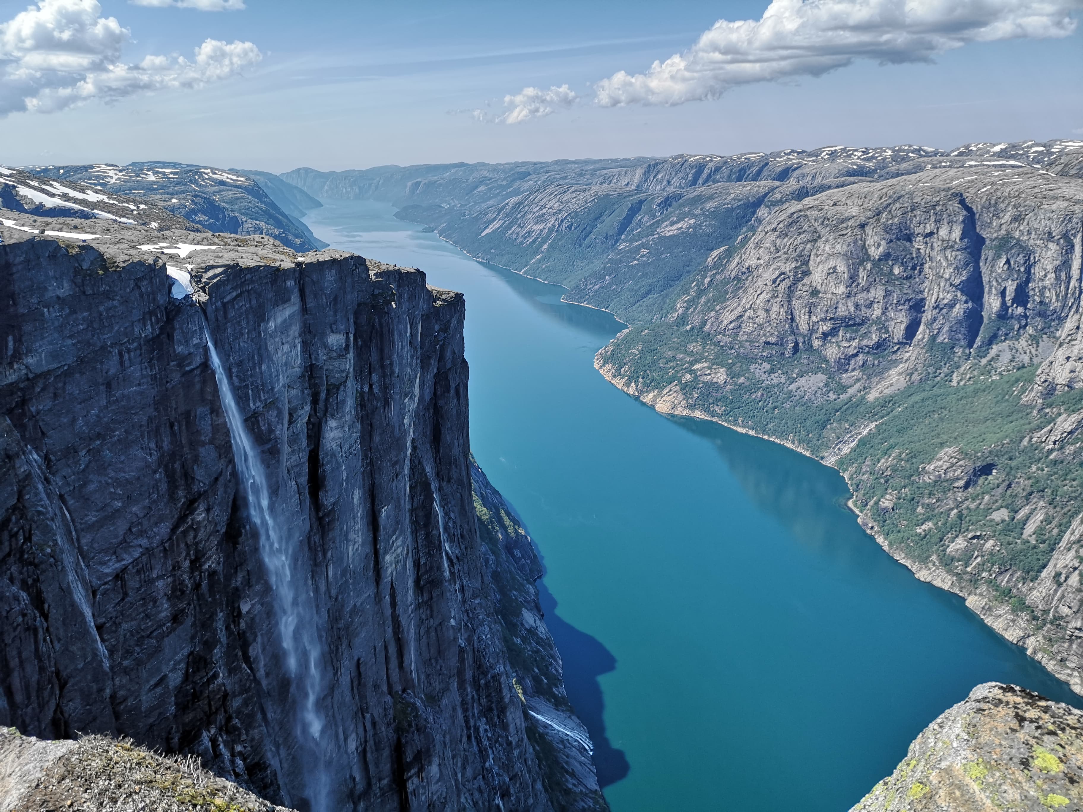 Fjellet Kjerag ruver over en knallblå fjord med fjell på hver side.