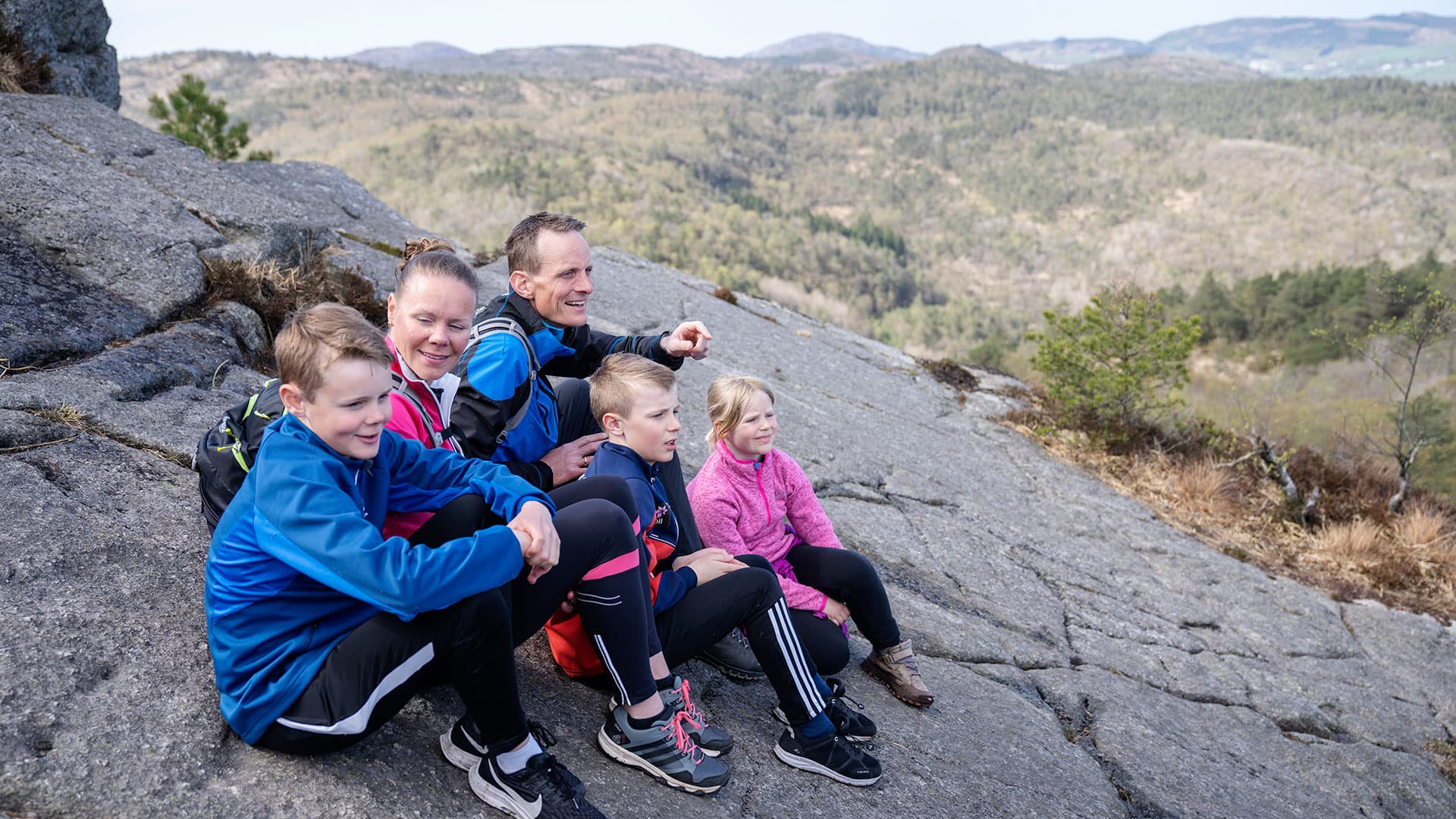En familie med tre barn som sitter på et fjell og ser på utsikten.