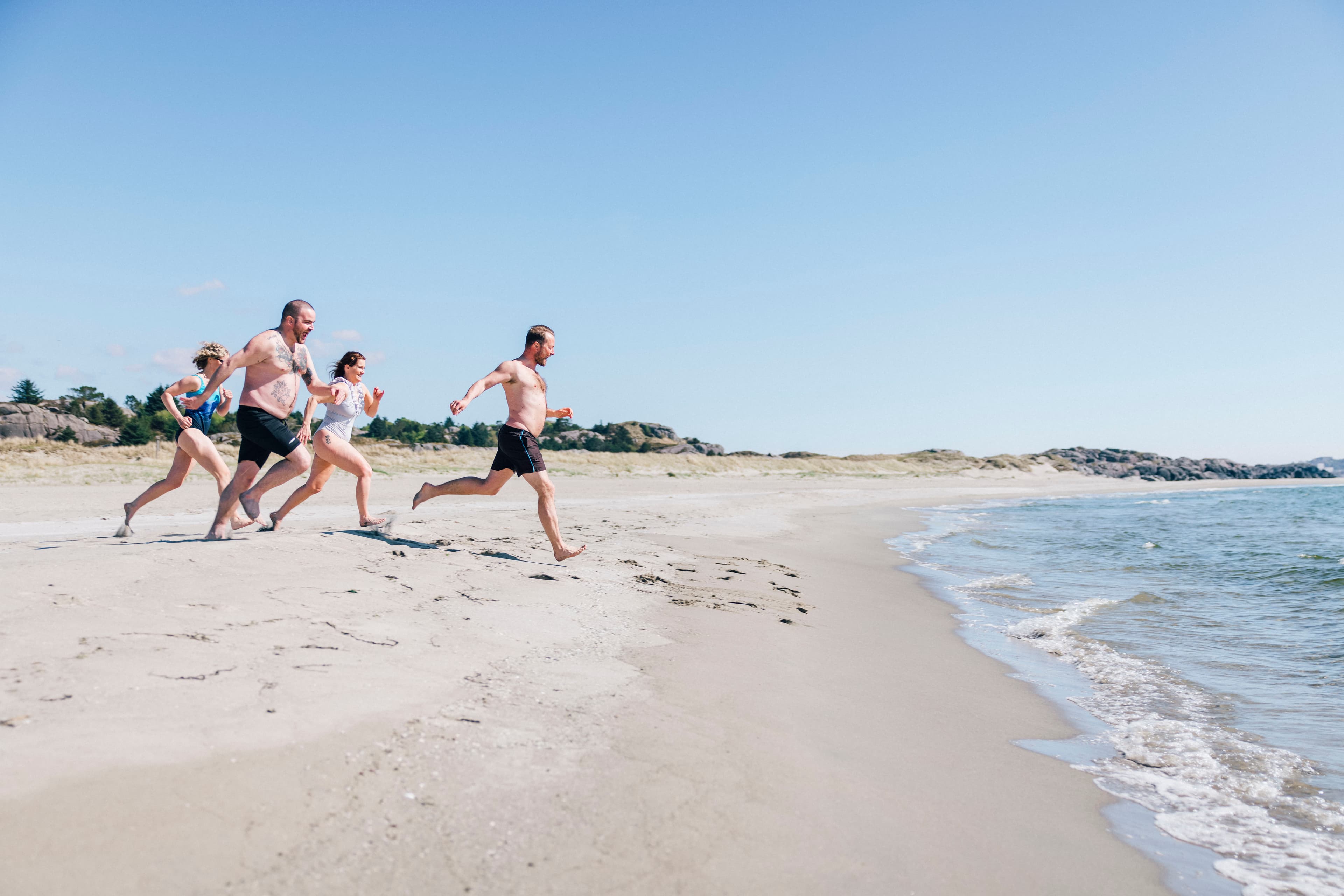 Fire personer løper mot havet i sanden for å bade.
