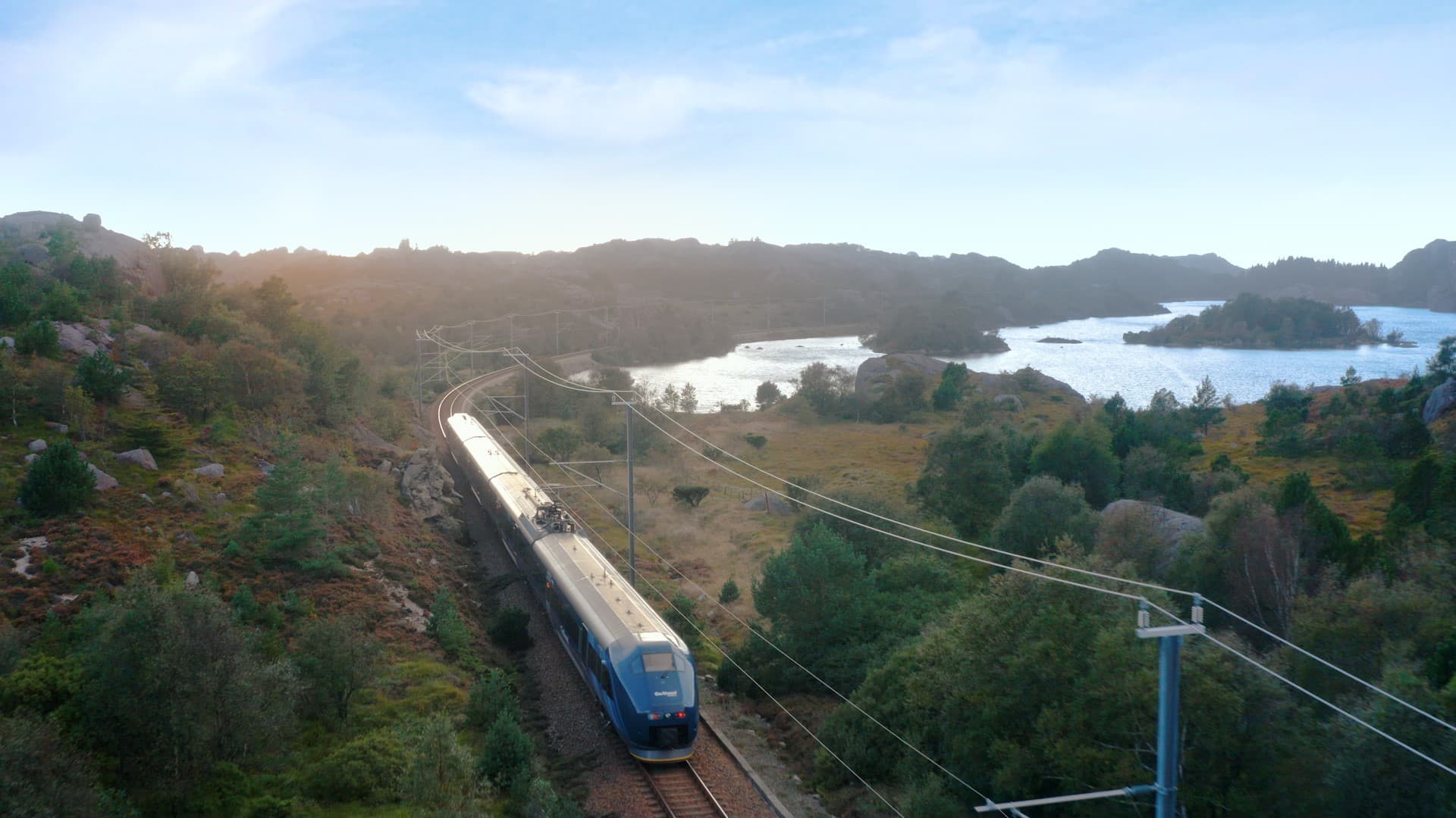 Tog sett fra luften i naturlandskap med grønt på en side og vann på en annen side.