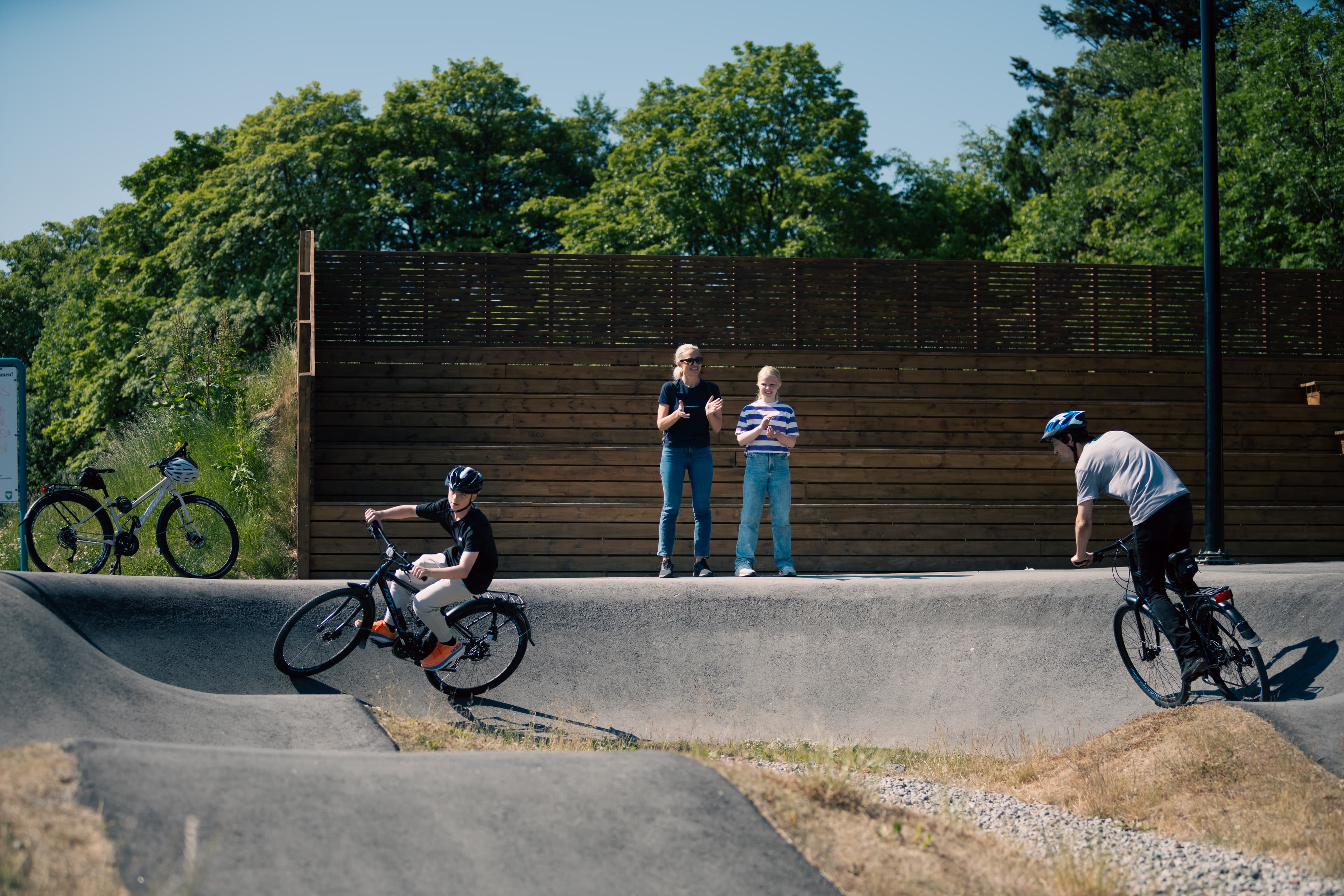 To barn sykler på pumptrackbane i Sandvedparken i Sandnes mens to personer står og ser på