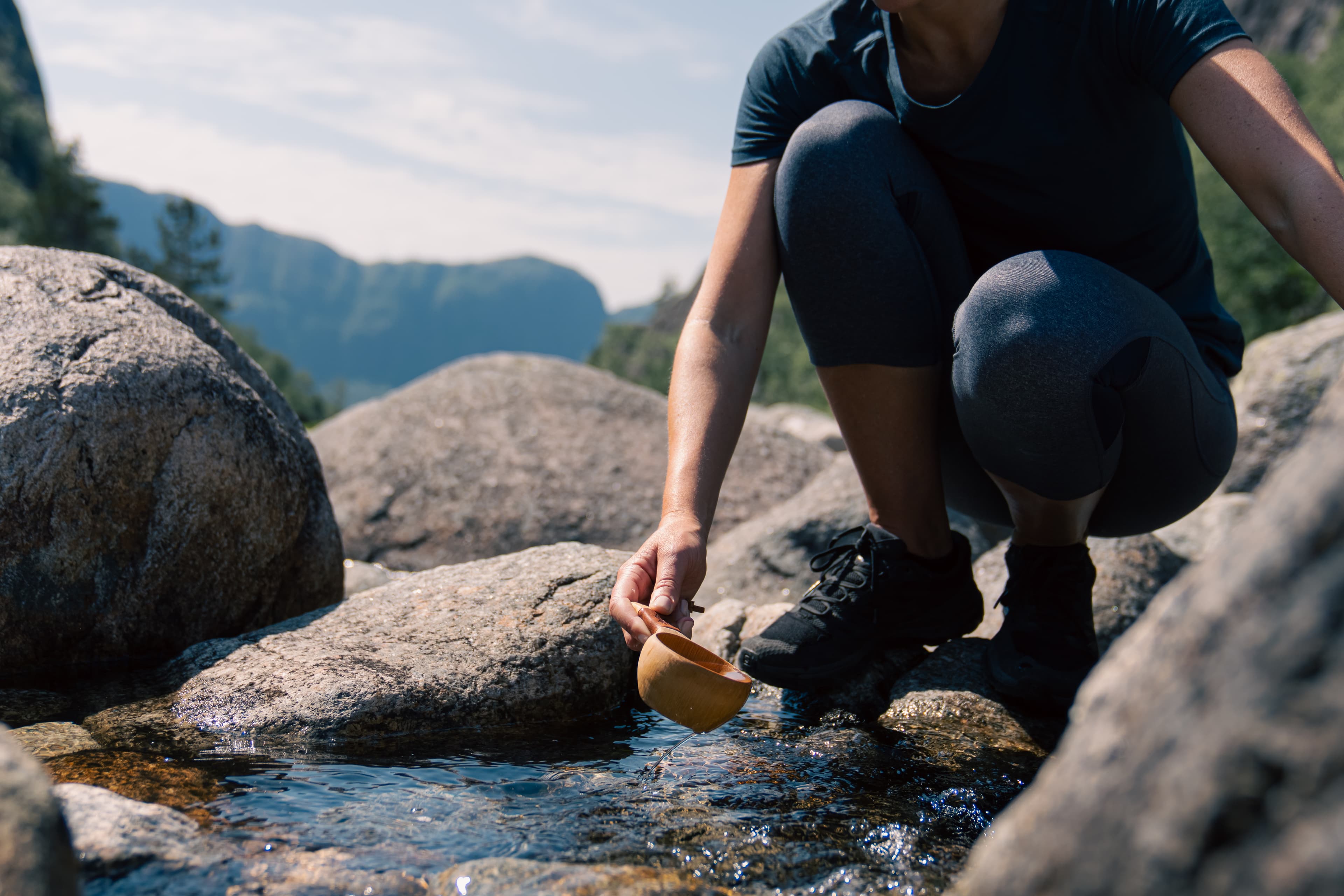 En kvinne som fylle opp koppen sin med vann fra en bekk i fjellet