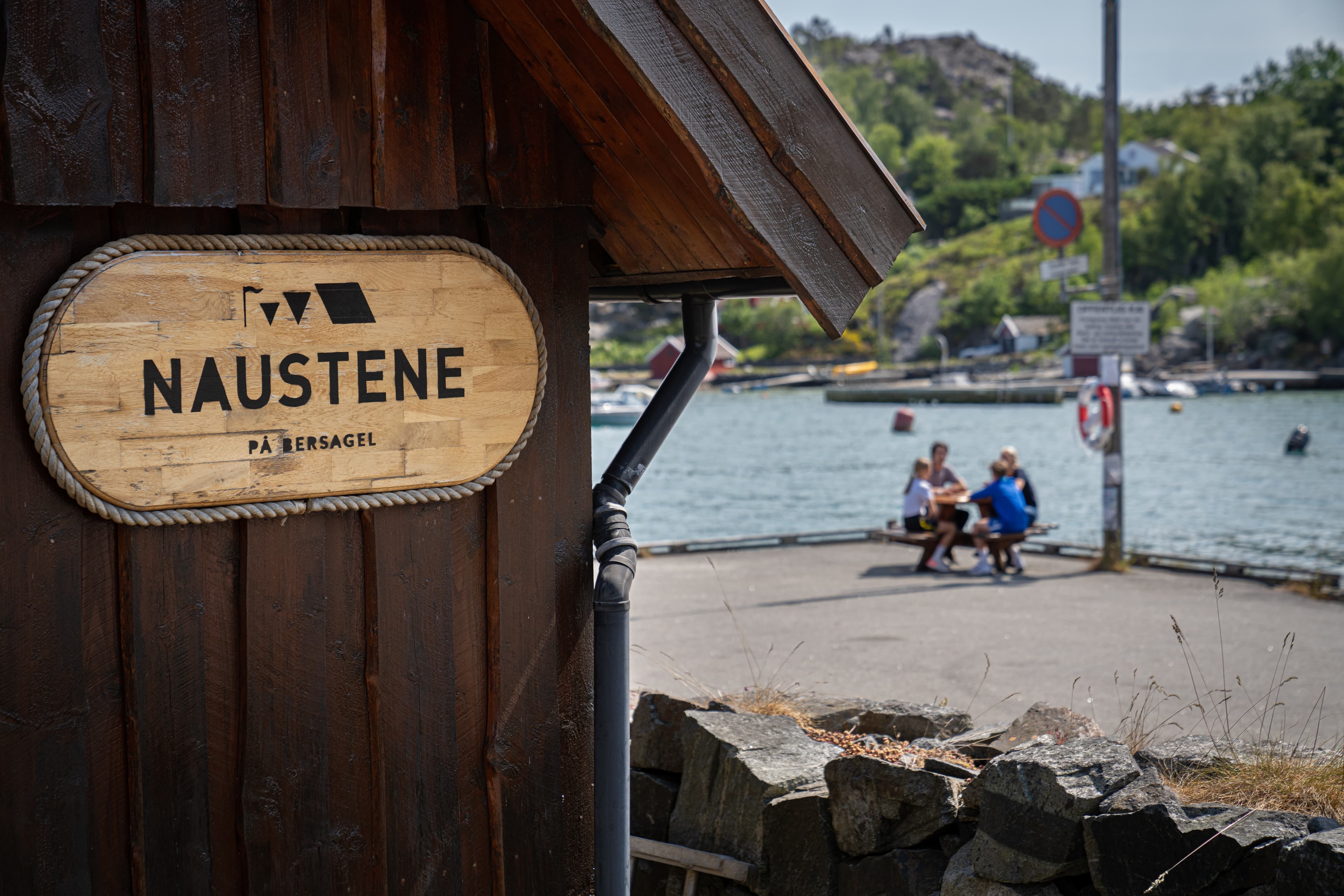 Naustene i Bersagel med en familie på brygge i bakgrunnen