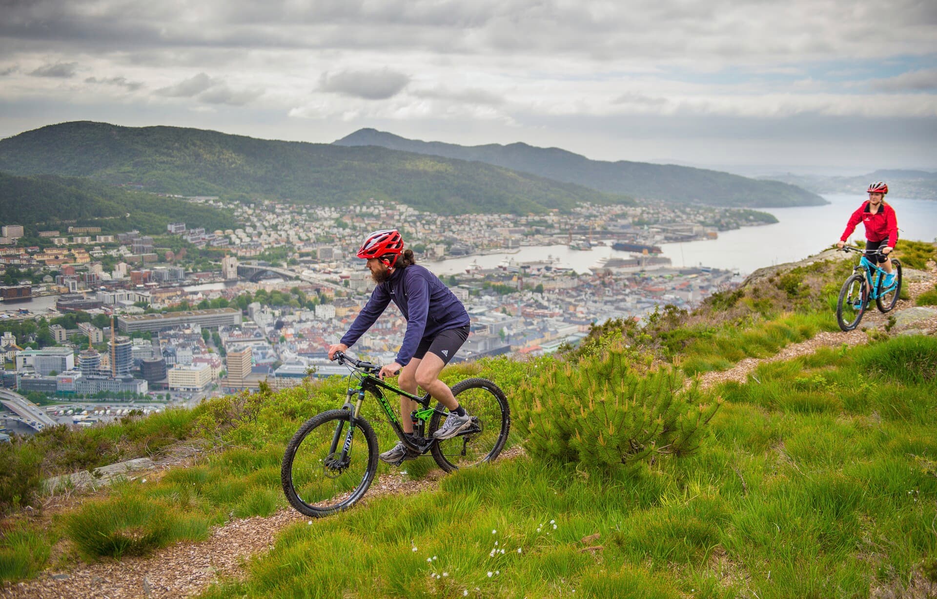 To personer som sykler på en sti med utsikt over Bergen by og Byfjorden.