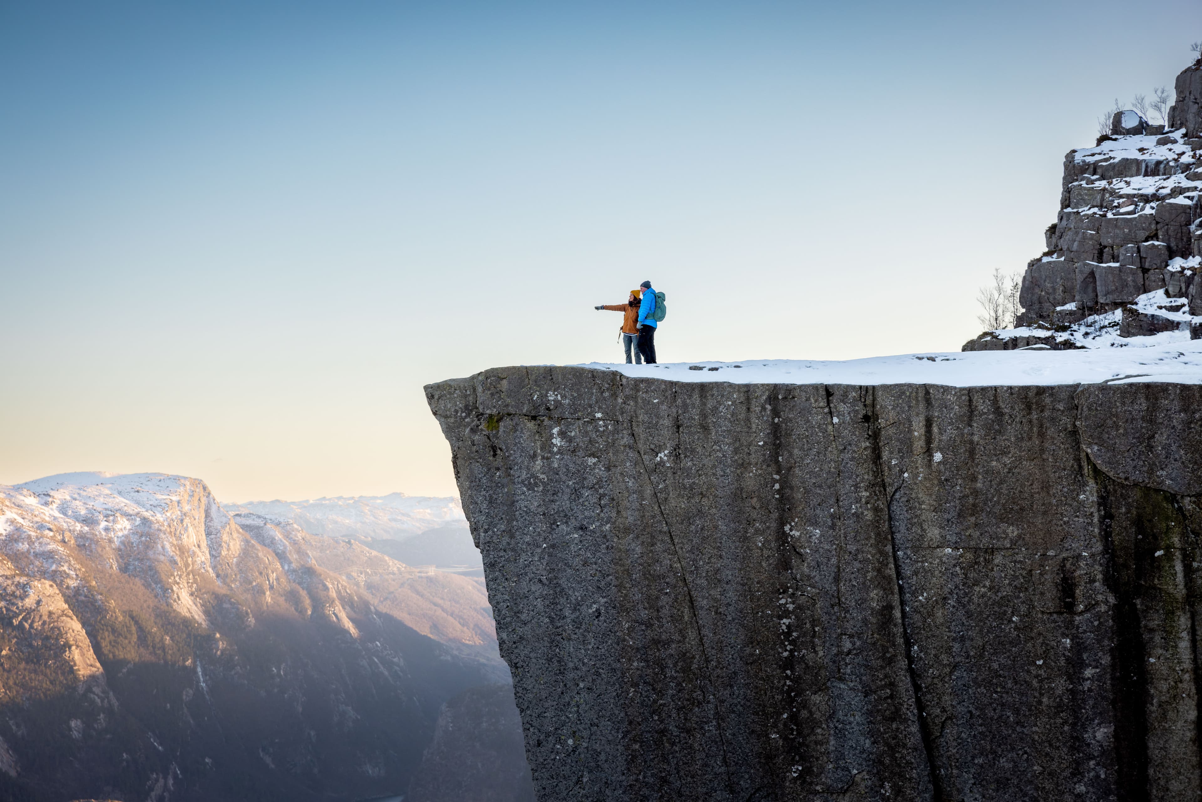 To personer som står på den snøkledde Preikestolen.