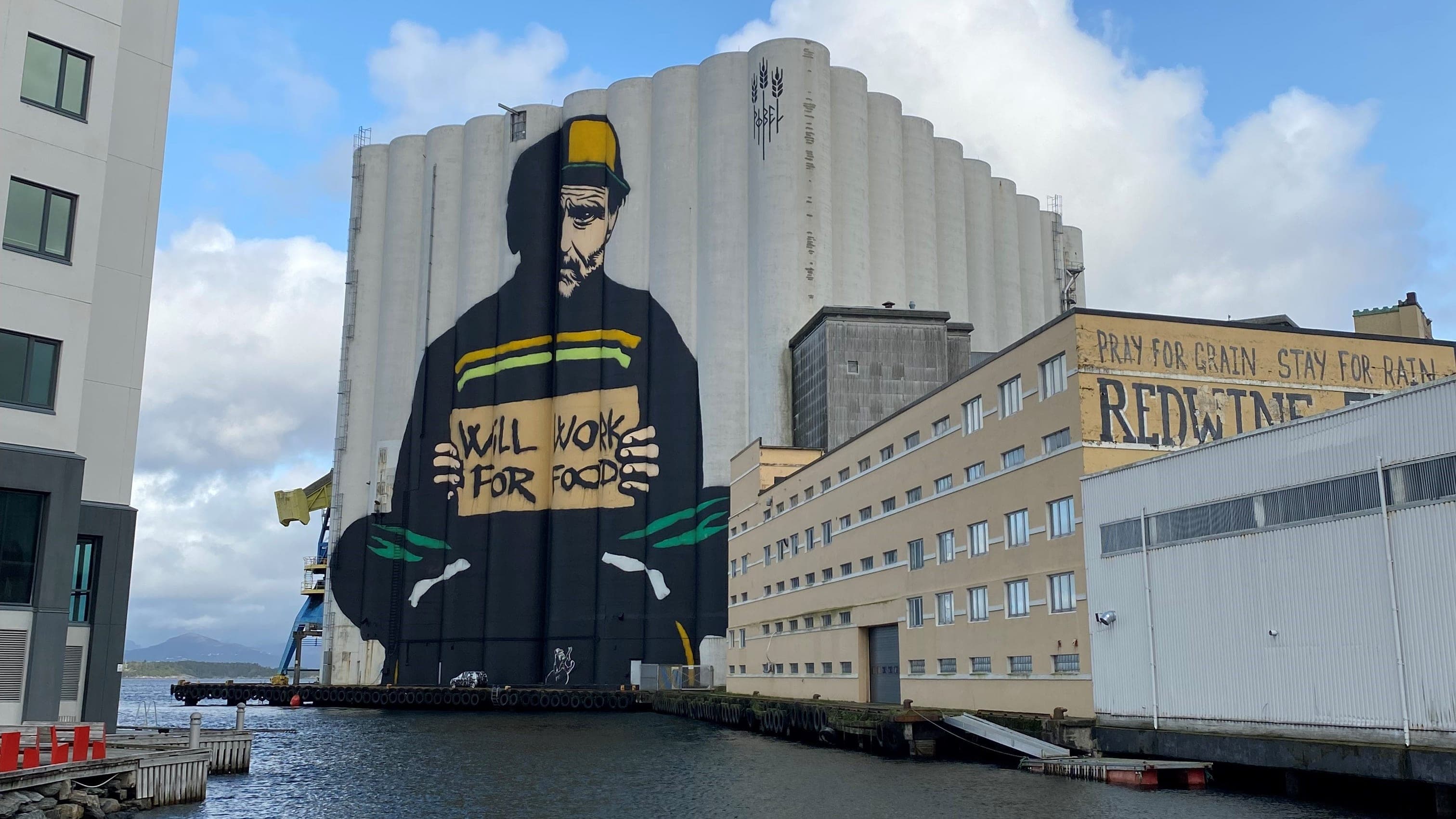 Street art work by Pøbel called will work for food. A farmer painted on two large silos.