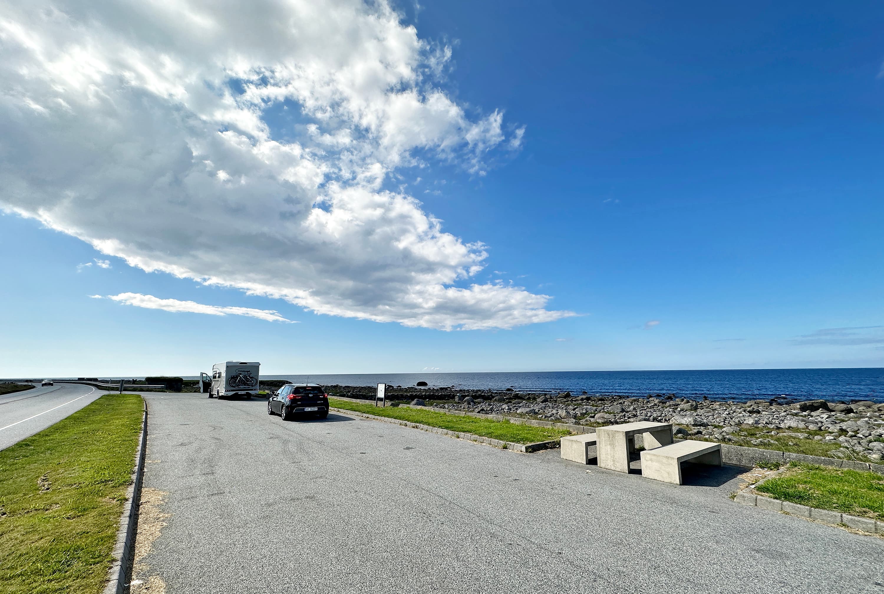A picnic area along the road with two cars parked. View of the open sea at Hårr rasteplass