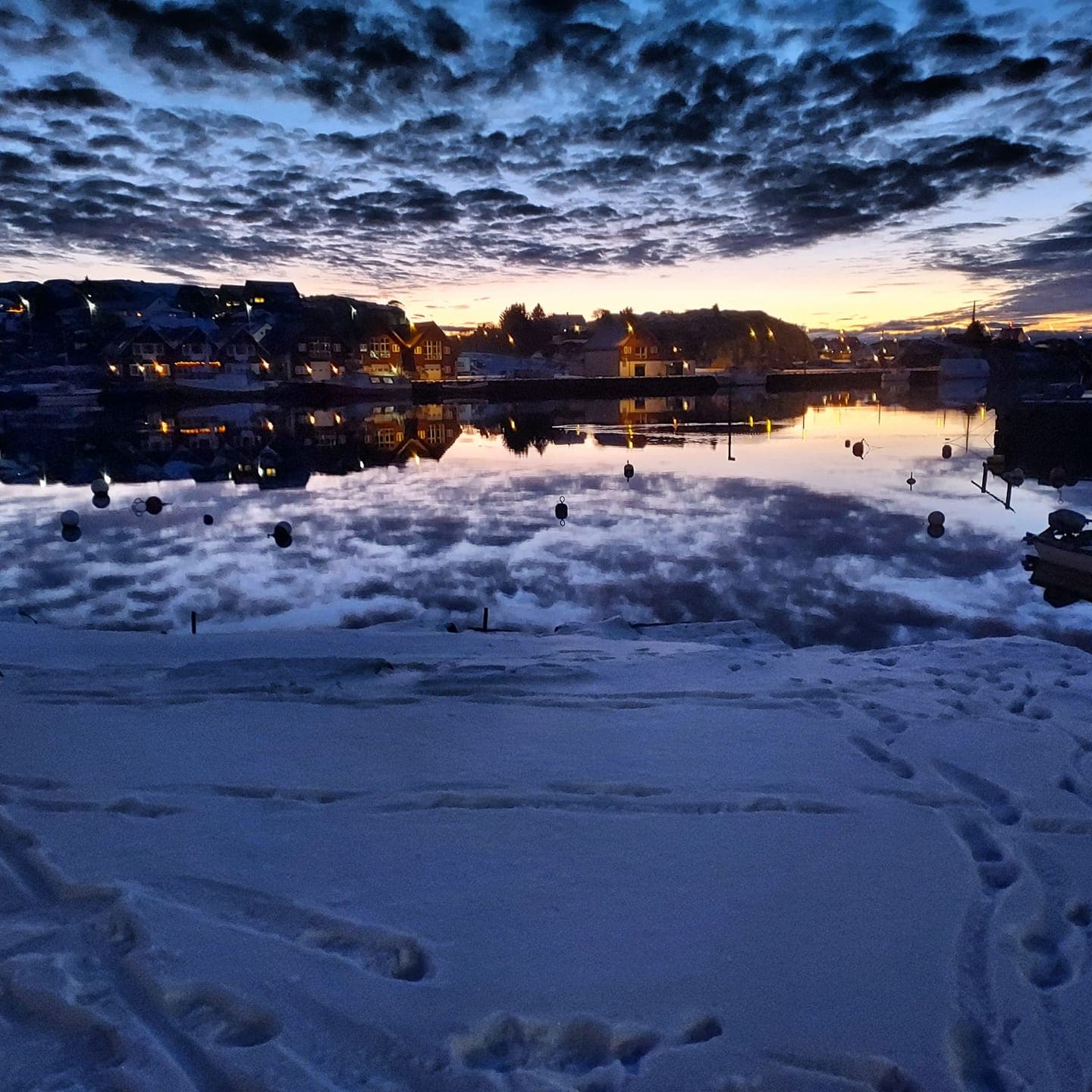 Sirevåg harbour with snow and evening light with yellow, orange and blue sky with clouds scattered over the harbour