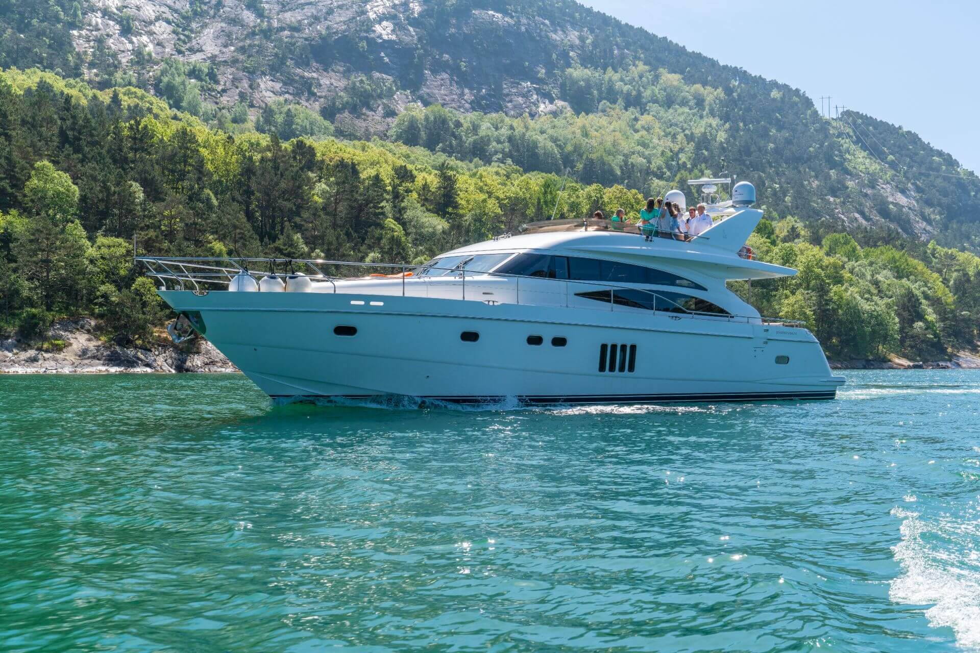 A white luxury yacht cruising the norwegian fjords with guests on board. Green vegetation behind the boat and mountains