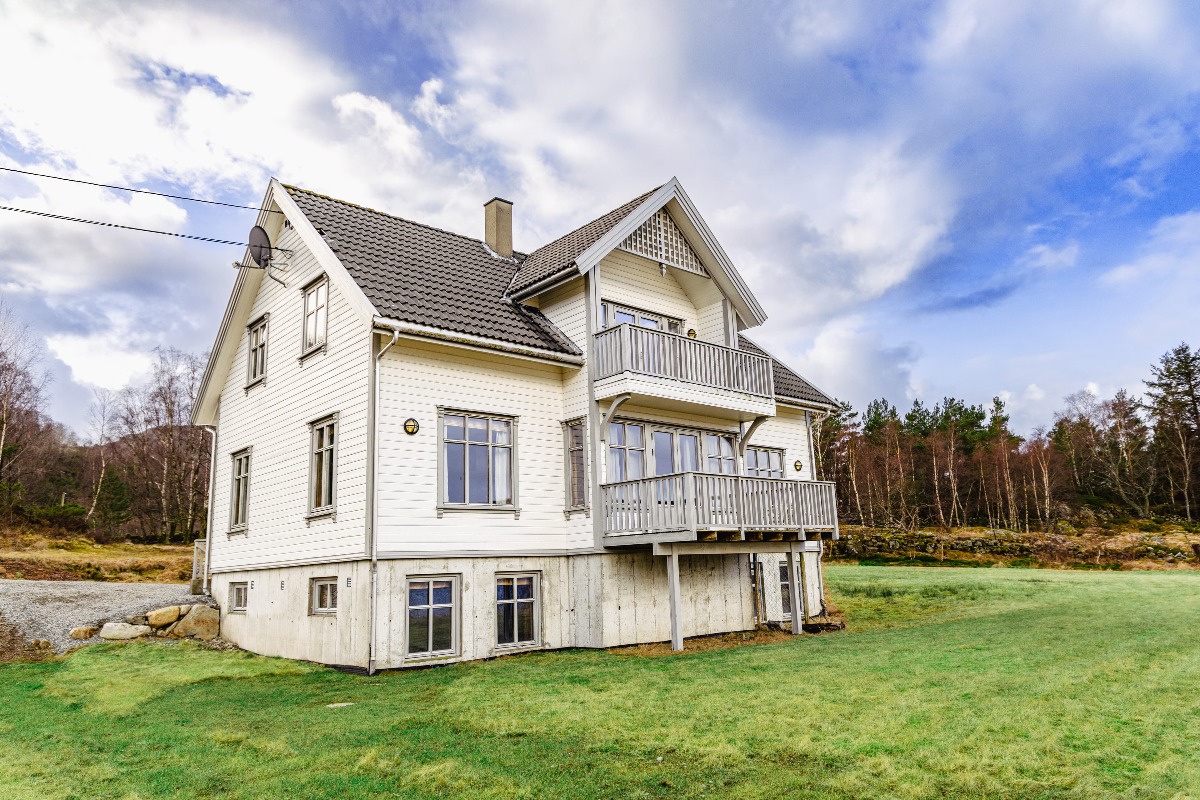 The facade of a holiday house near Preikestolen. White, wooden house over several floors. Surrounded by green grass and some trees behind the house.