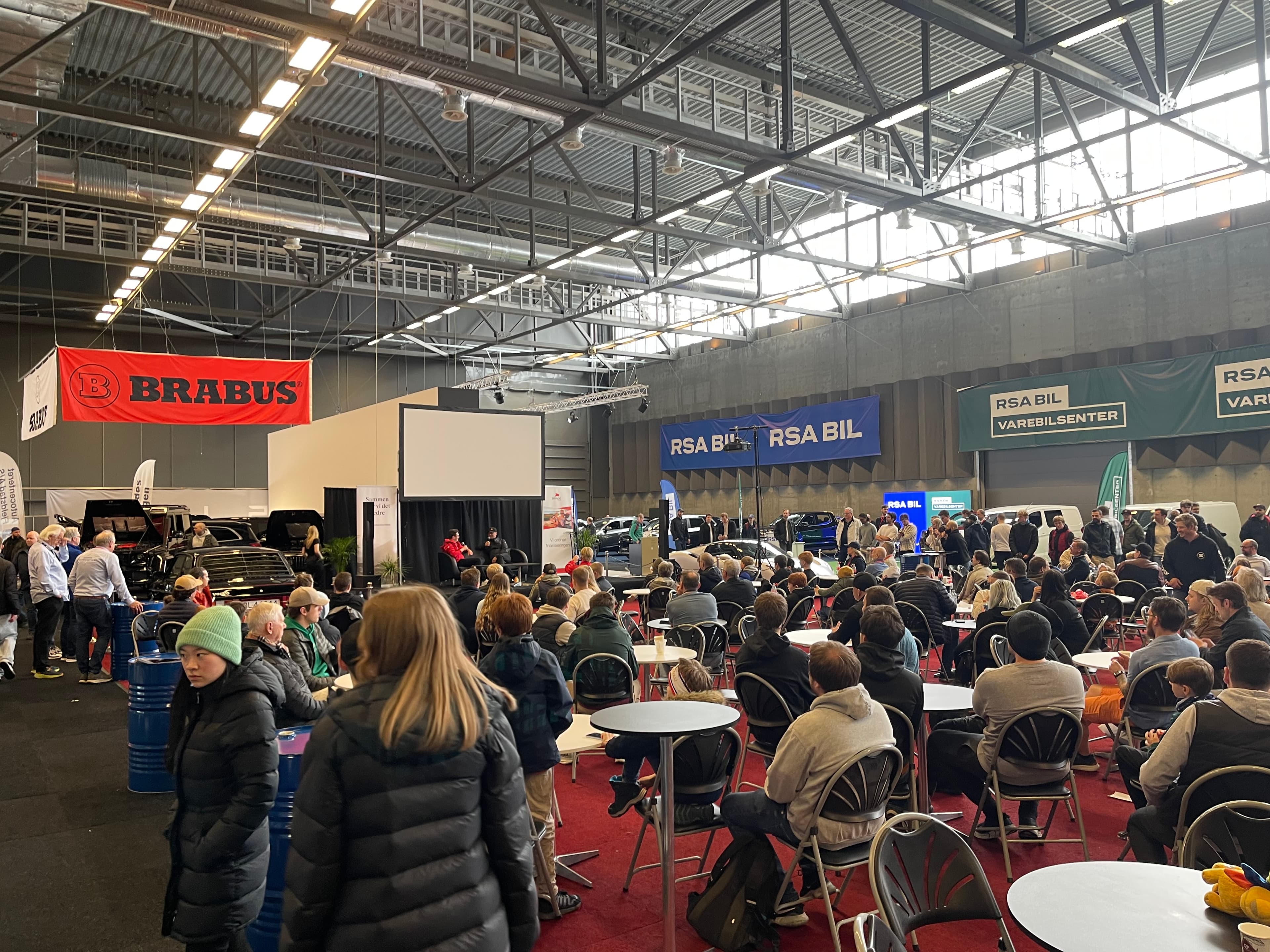 lots of people in an expo hall with cars and motorbikes
