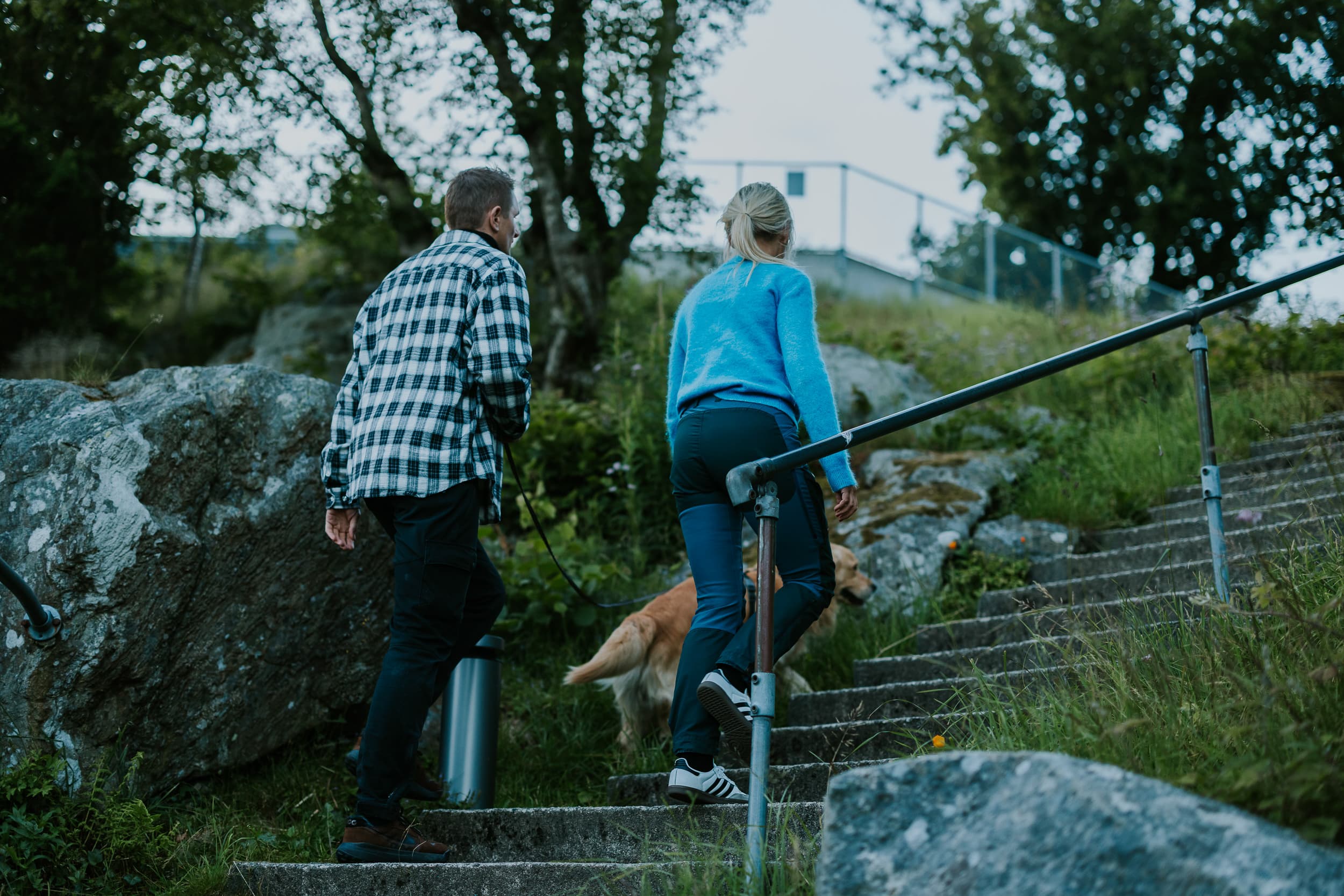 Two people and a dog walking up the stairs to the mountain Hanafjellet. The stairs are called Hanatrappene. From the top the view shows Sandnes and fjord