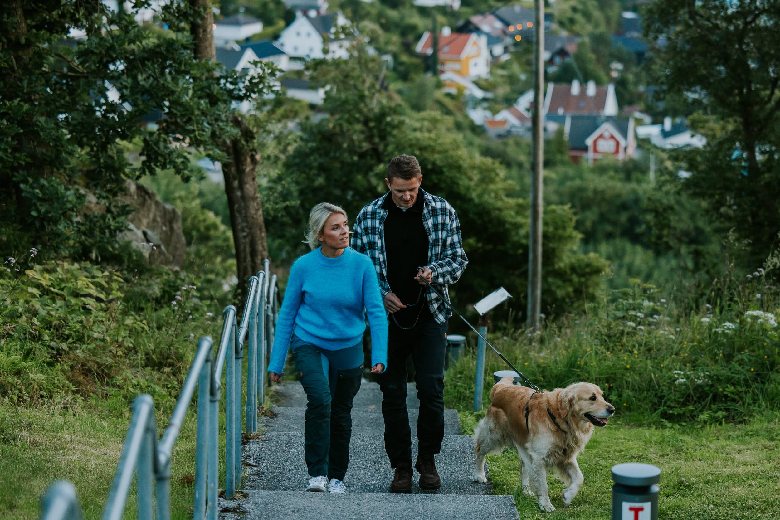 Two people and a dog walking up the stairs to the mountain Hanafjellet. The stairs are called Hanatrappene. From the top the view shows Sandnes and fjord