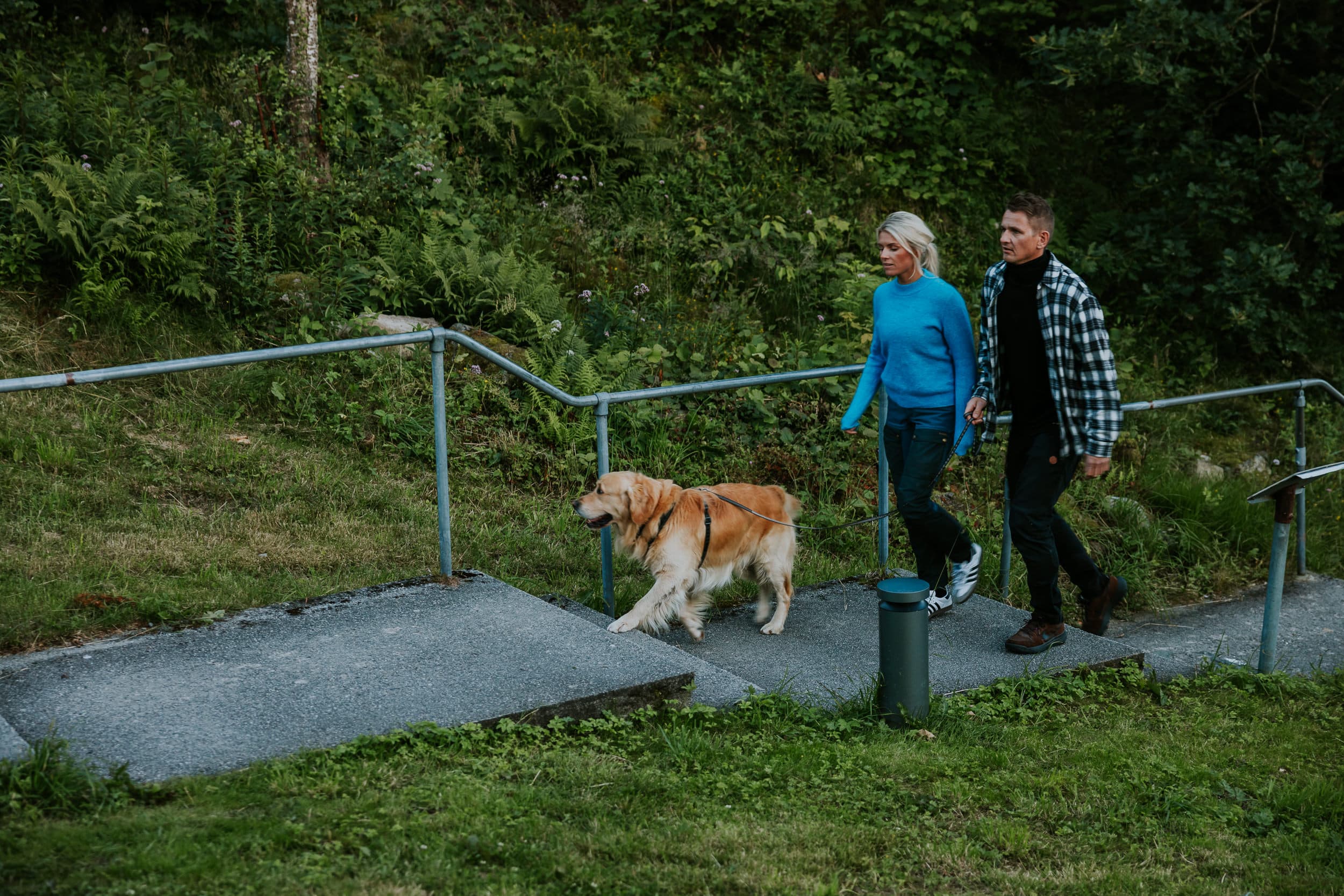 Two people and a dog walking up the stairs to the mountain Hanafjellet. The stairs are called Hanatrappene. From the top the view shows Sandnes and fjord