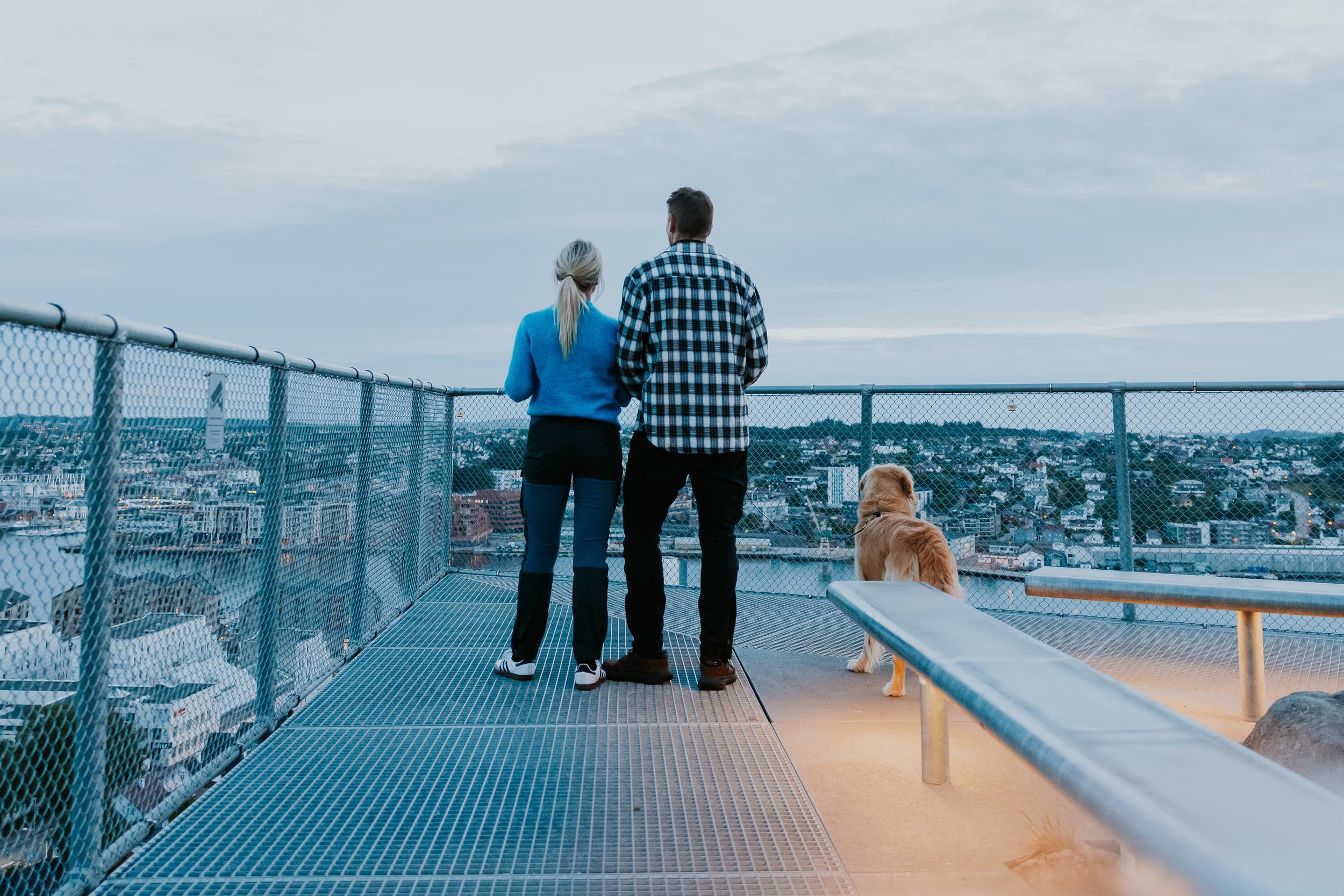 Two people and a dog walking up the stairs to the mountain Hanafjellet. The stairs are called Hanatrappene. From the top the view shows Sandnes and fjord