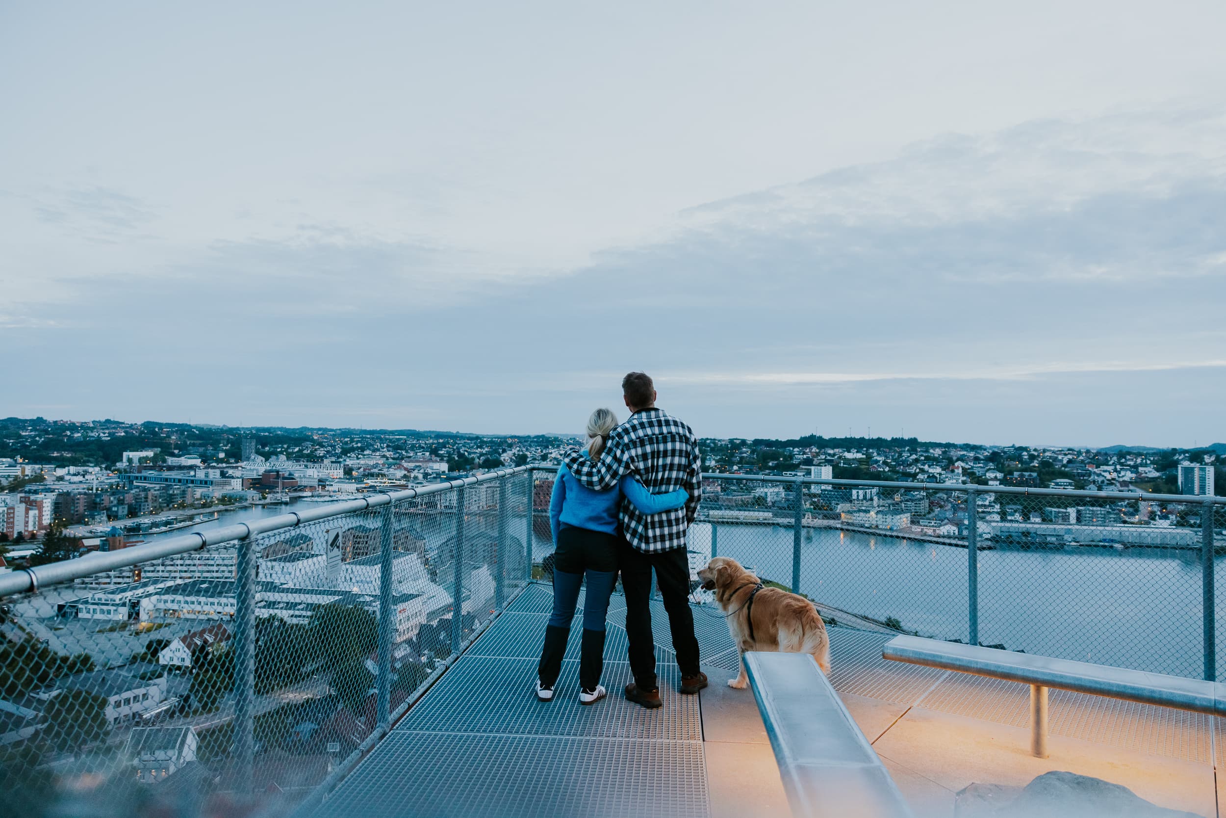 Two people and a dog walking up the stairs to the mountain Hanafjellet. The stairs are called Hanatrappene. From the top the view shows Sandnes and fjord