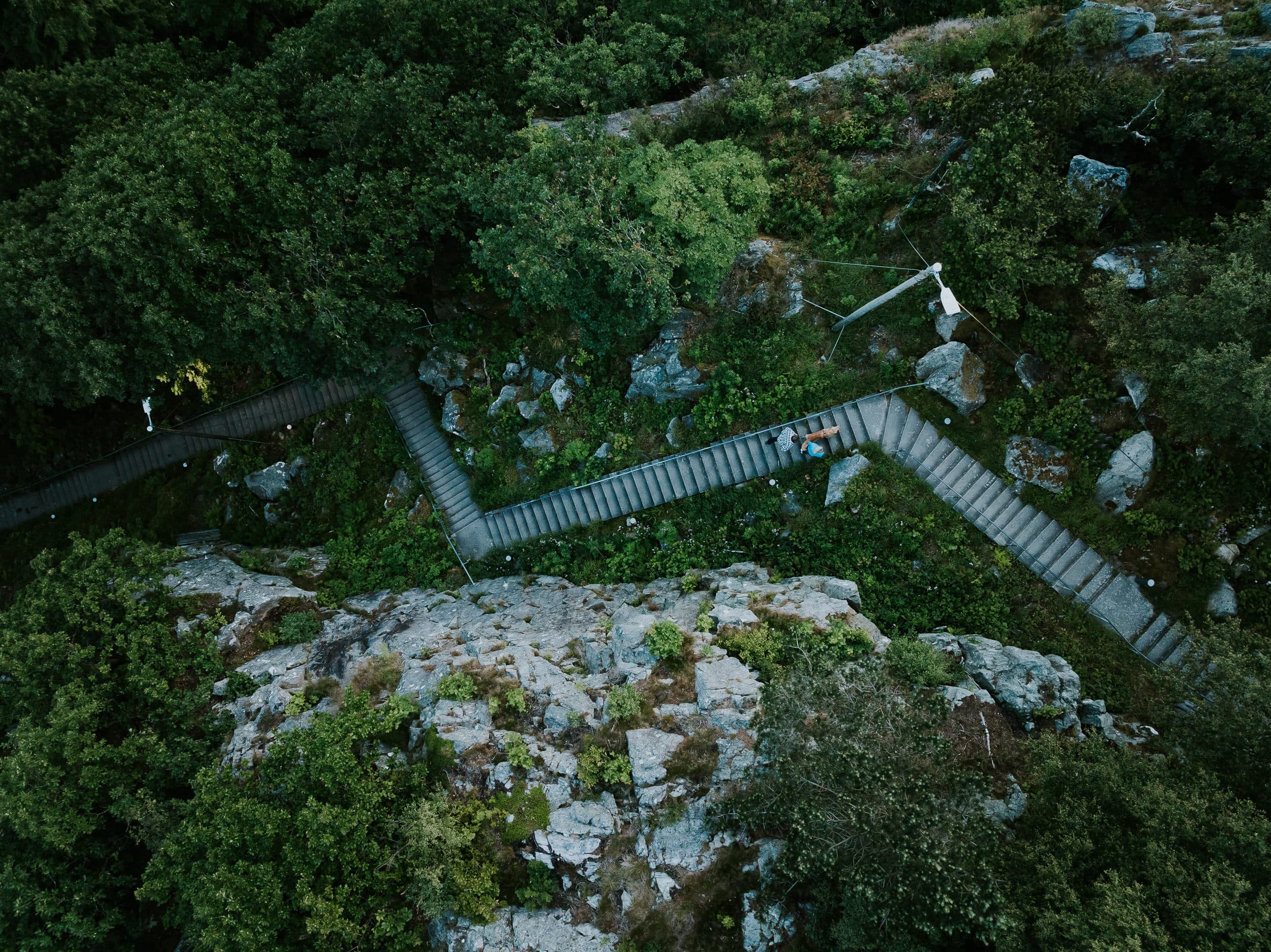 Two people and a dog walking up the stairs to the mountain Hanafjellet. The stairs are called Hanatrappene. From the top the view shows Sandnes and fjord